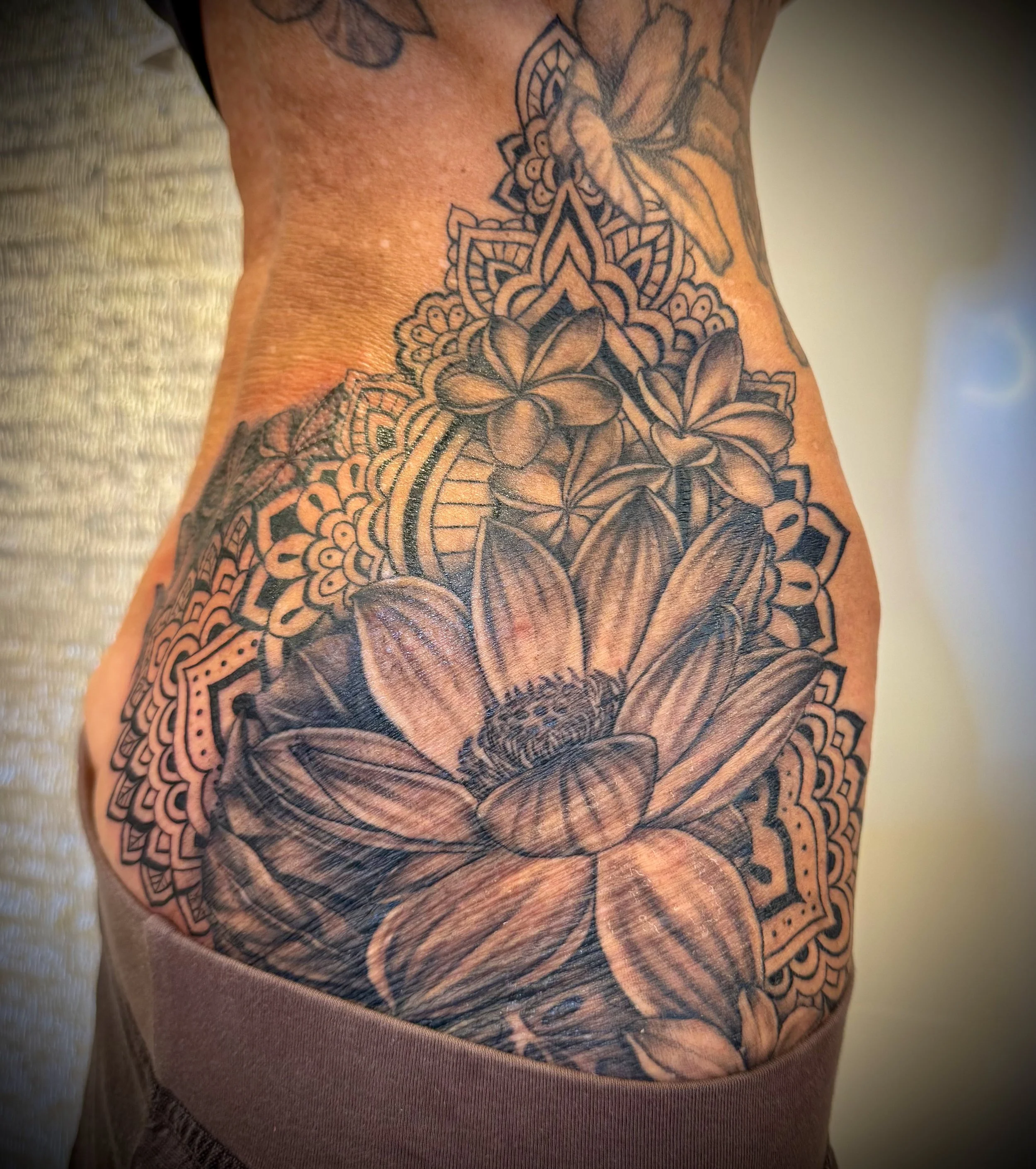 Close-up of a person's side torso featuring a detailed black and gray floral tattoo design.