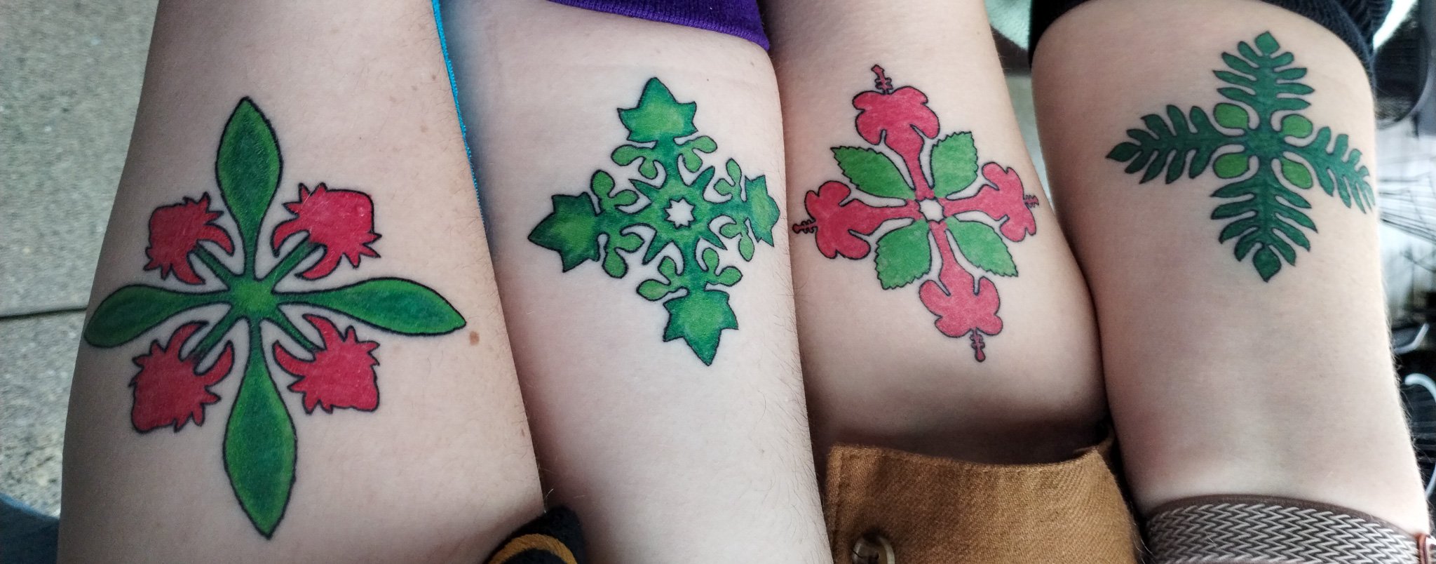 Four people with matching tattoos of holiday-themed holly and Christmas plant designs on their upper arms.