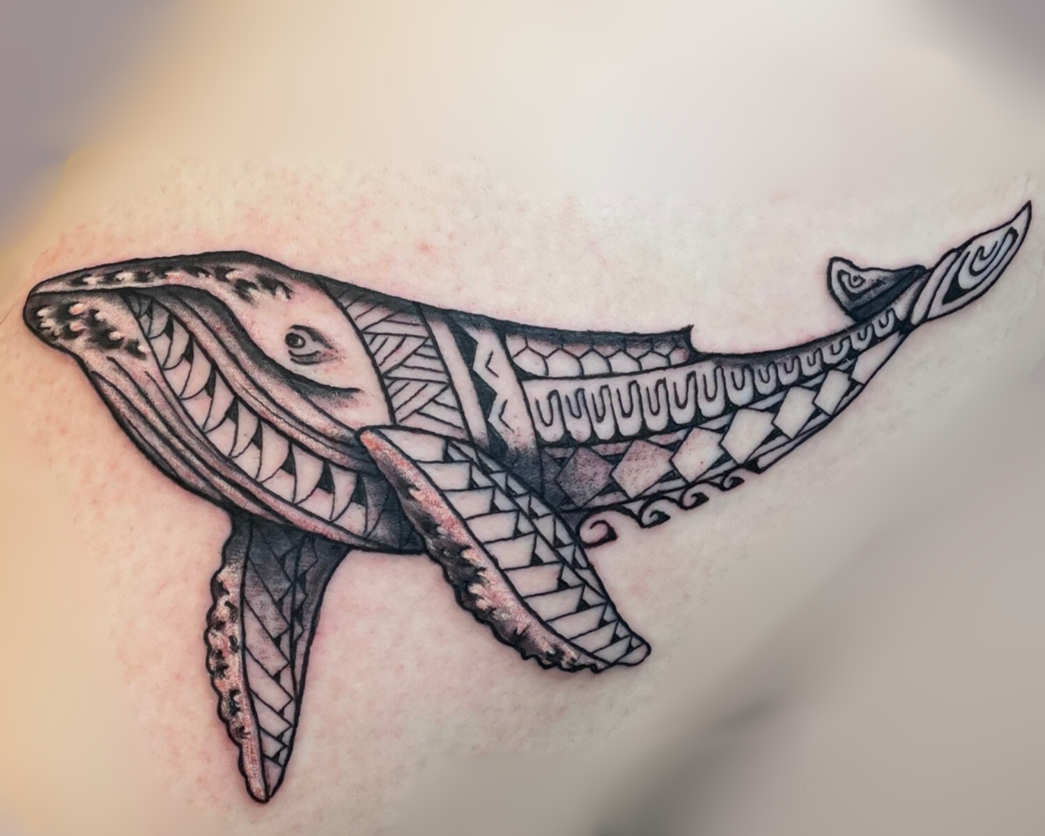 Black and grey Polynesian-style whale tattoo featuring geometric tribal patterns, detailed linework, and flowing traditional Hawaiian-inspired design across the body and fins
