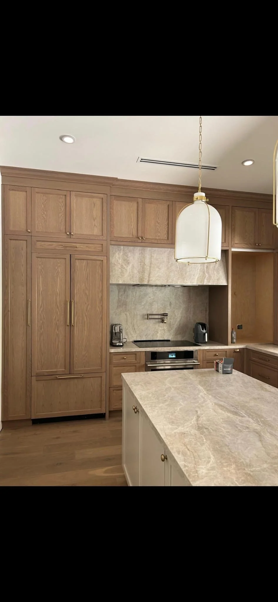 Kitchen with wooden cabinets, marble backsplash, and an island with marble countertop. Contains modern appliances and pendant lighting.