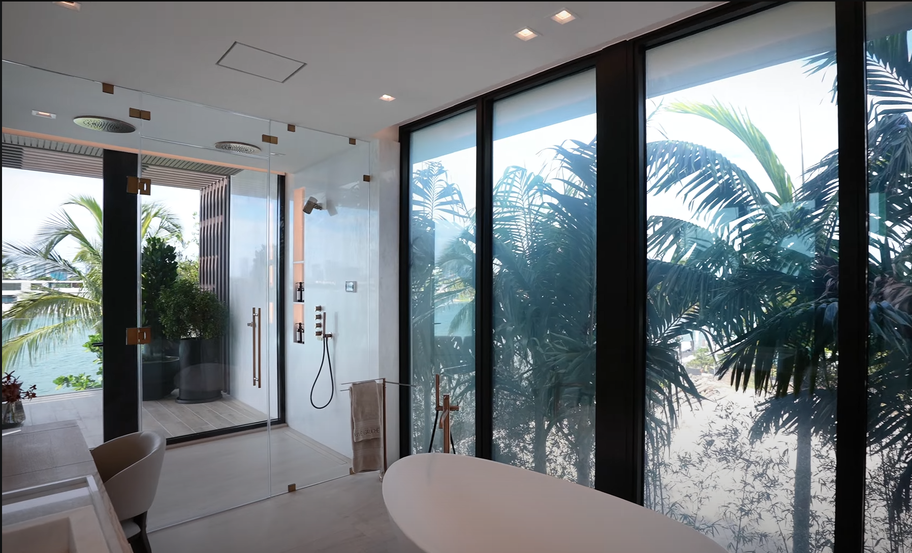 Modern indoor shower with glass door and tropical view outside, featuring jungle plants and trees.