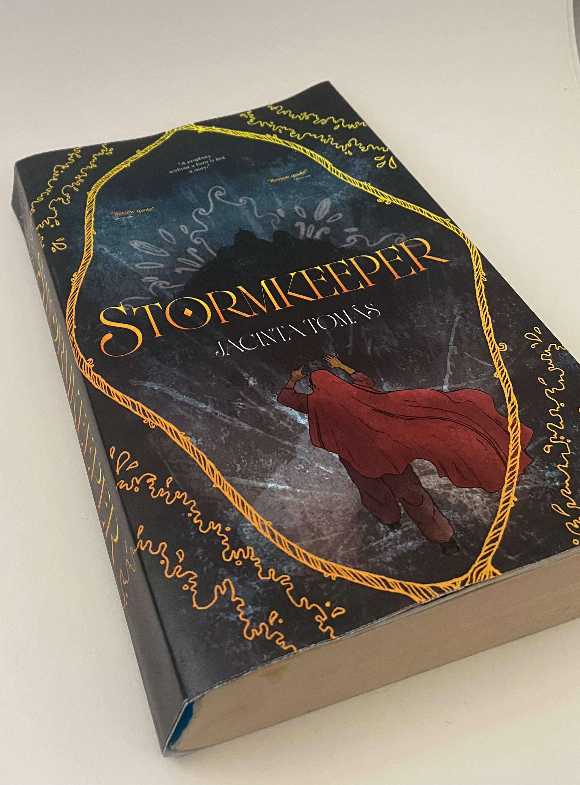A paperback book titled 'Stormkeeper' by Jacquelyn Mitchard, with a cover illustration of a woman in a red dress reaching towards the sky, surrounded by swirling patterns and a dark, mountainous landscape background.