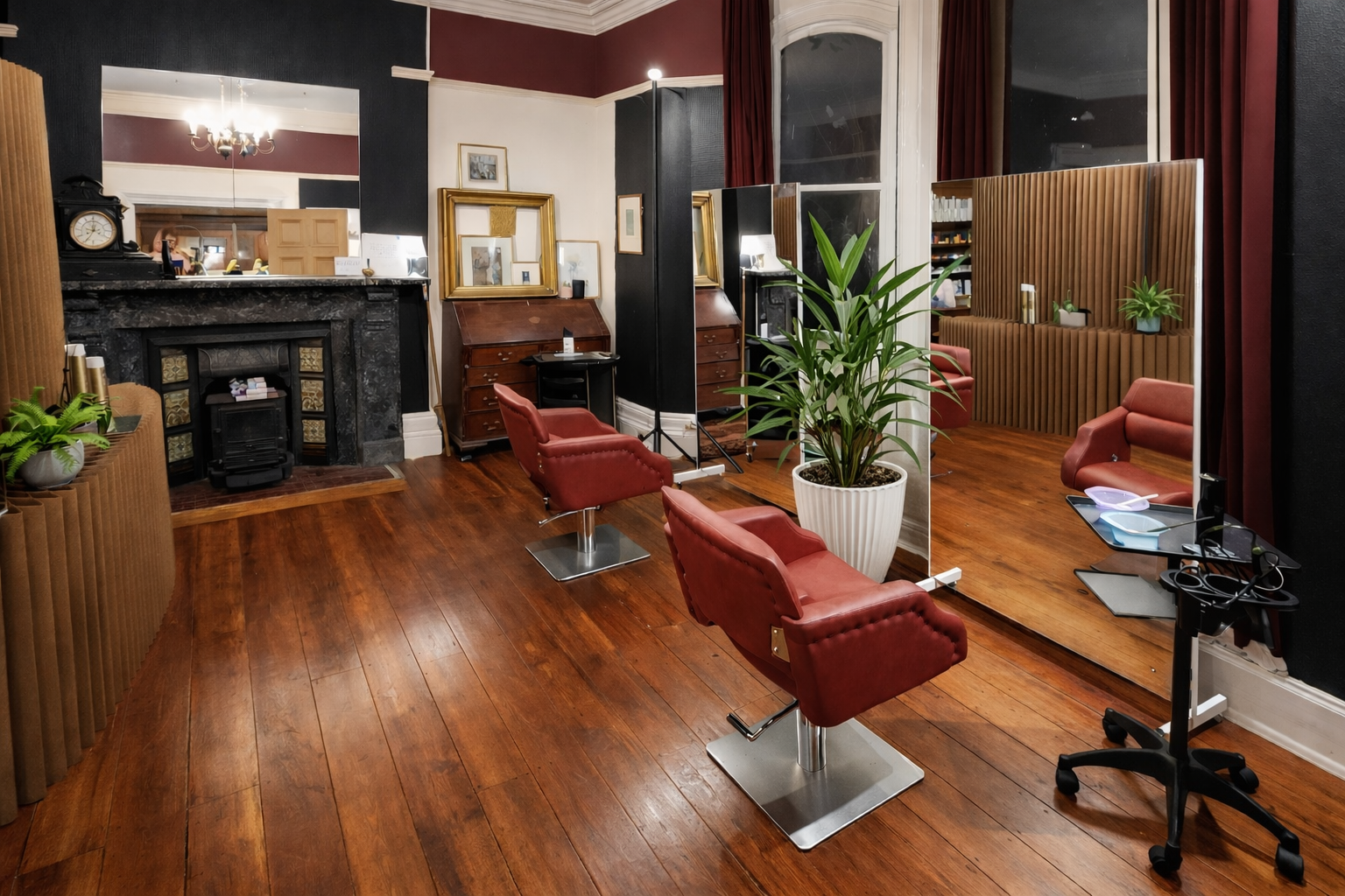 A vintage hair salon with wooden floors, red chairs, a large mirror, and a plant in a white pot.