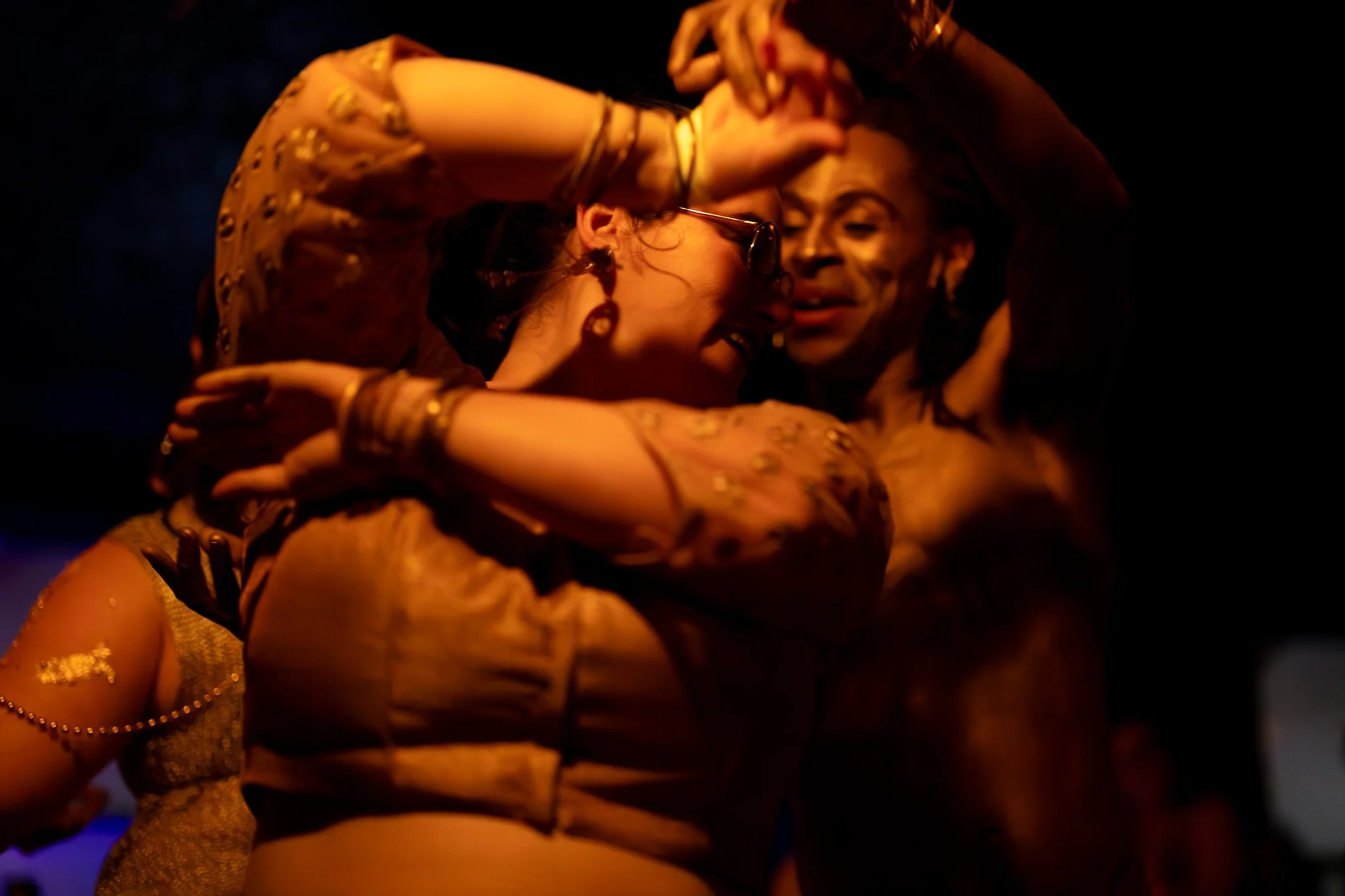 Two women dancing closely together in a dimly lit environment, smiling and embracing each other.