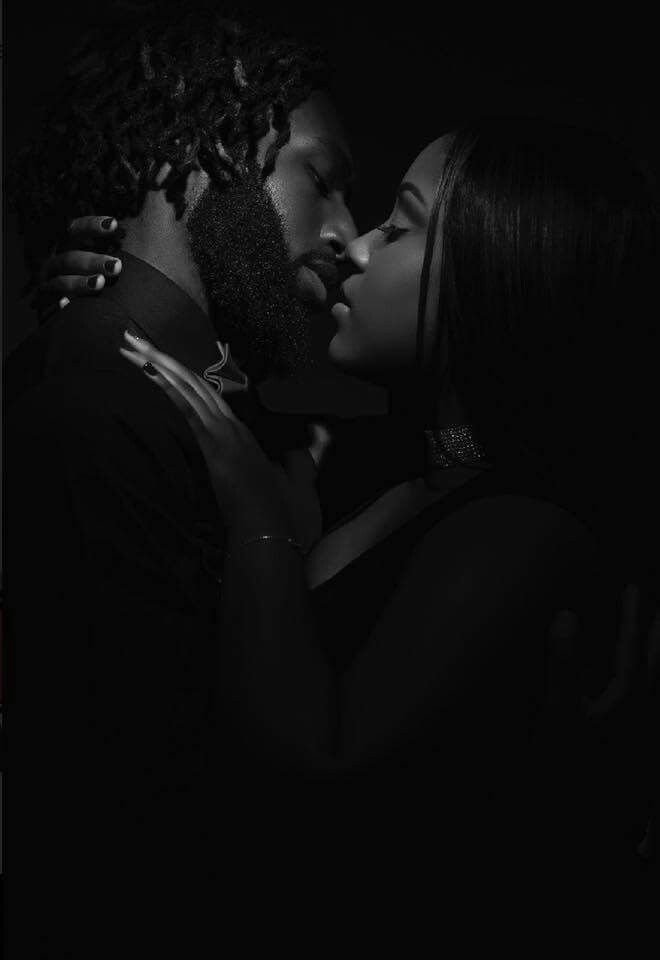 A black and white photo of a man and woman holding each other close, about to kiss in a dark setting.