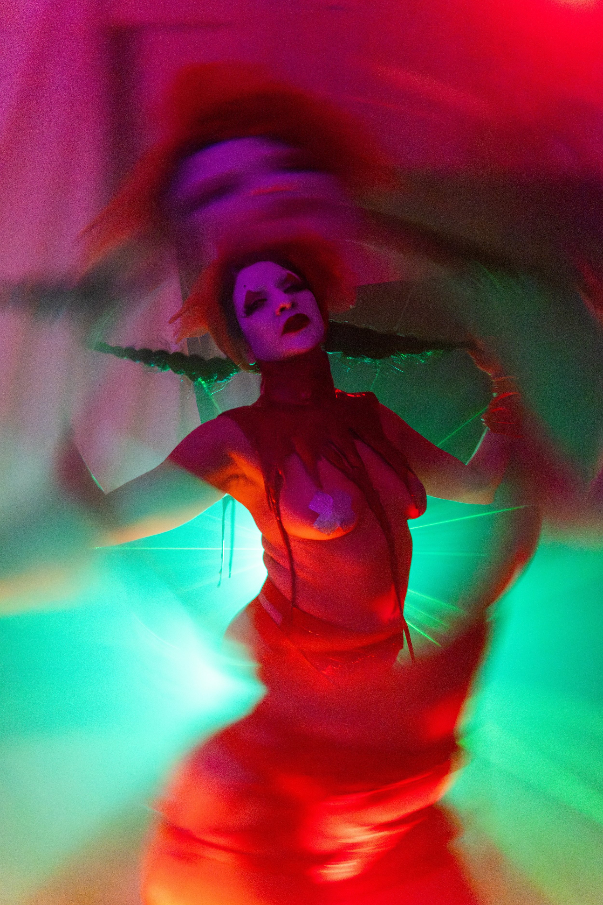 Person dressed in a red costume with makeup, neon lights, vivid colors, and blurred motion.