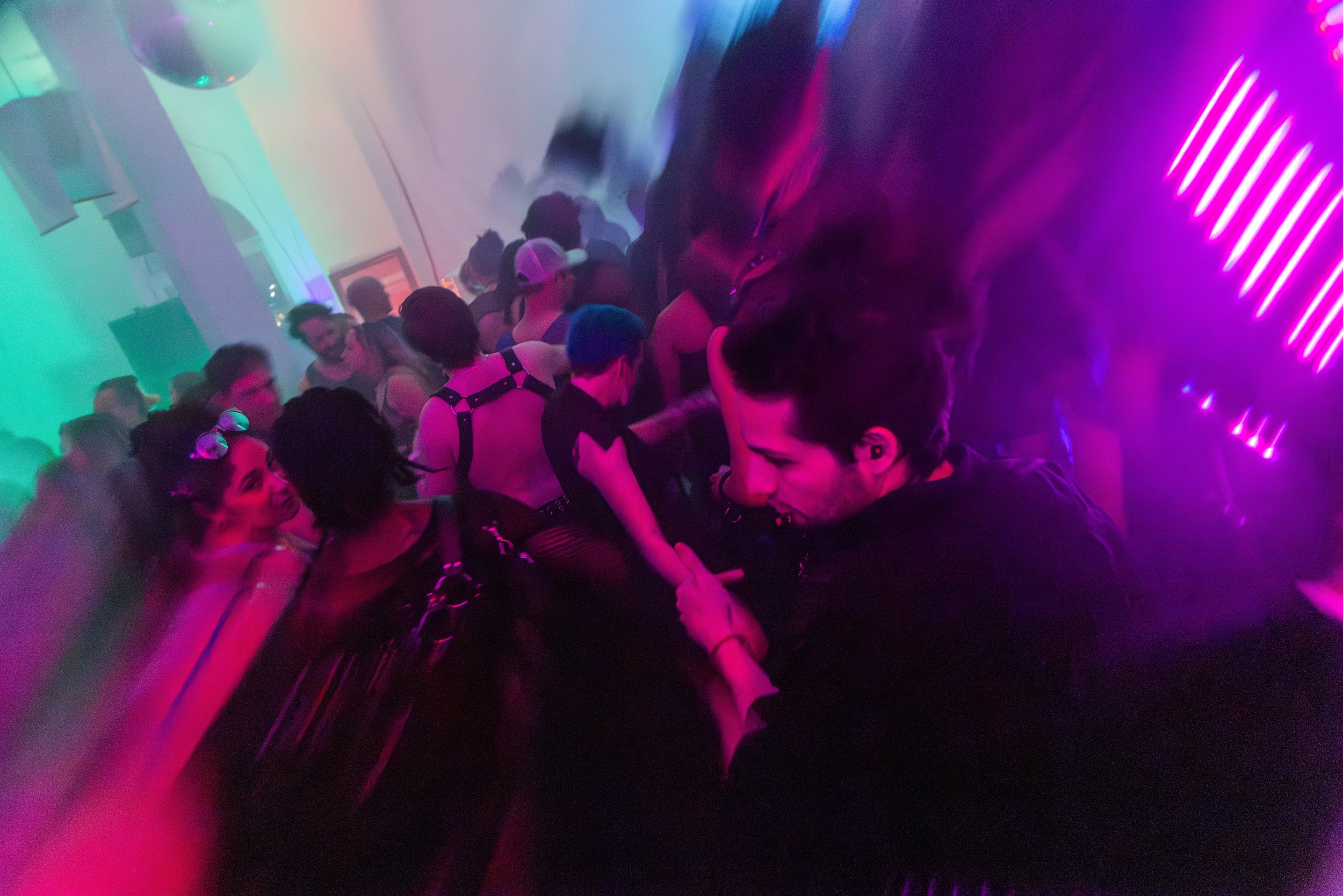 Crowd dancing and socializing at a neon-lit nightclub with colorful lights and fog.