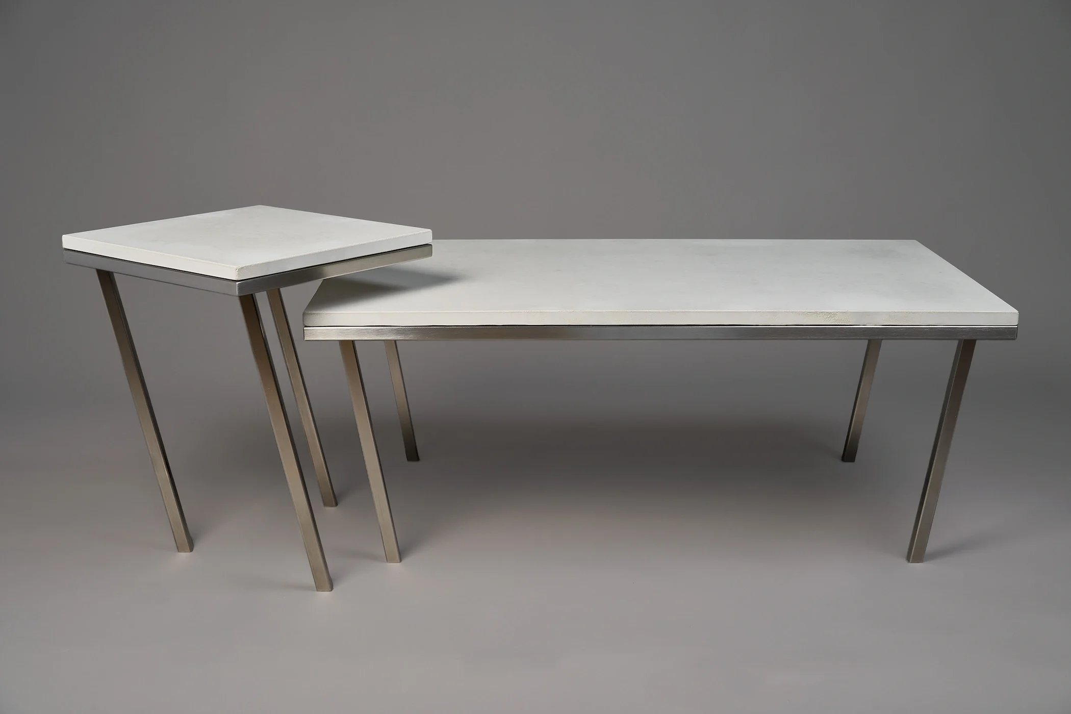 A set of three nested tables with white marble topsand angled metal legs against a gray background.