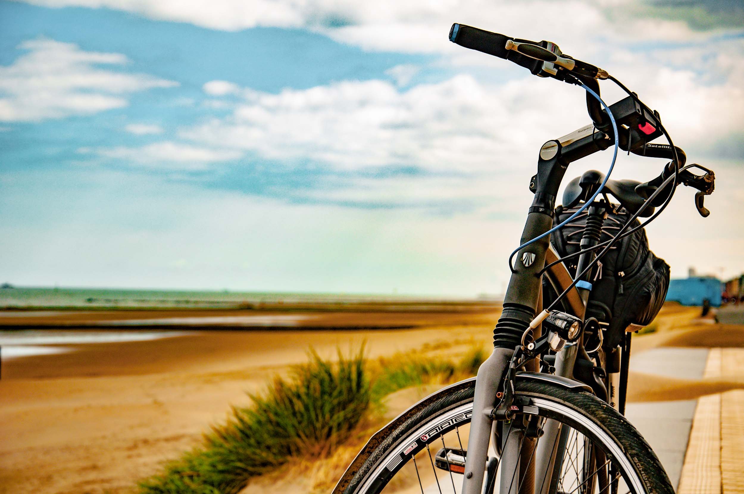 Close-up of a black bicycle parked on a paved pathway next to the North Sea in Ostende, a blue sky with clouds in the background.