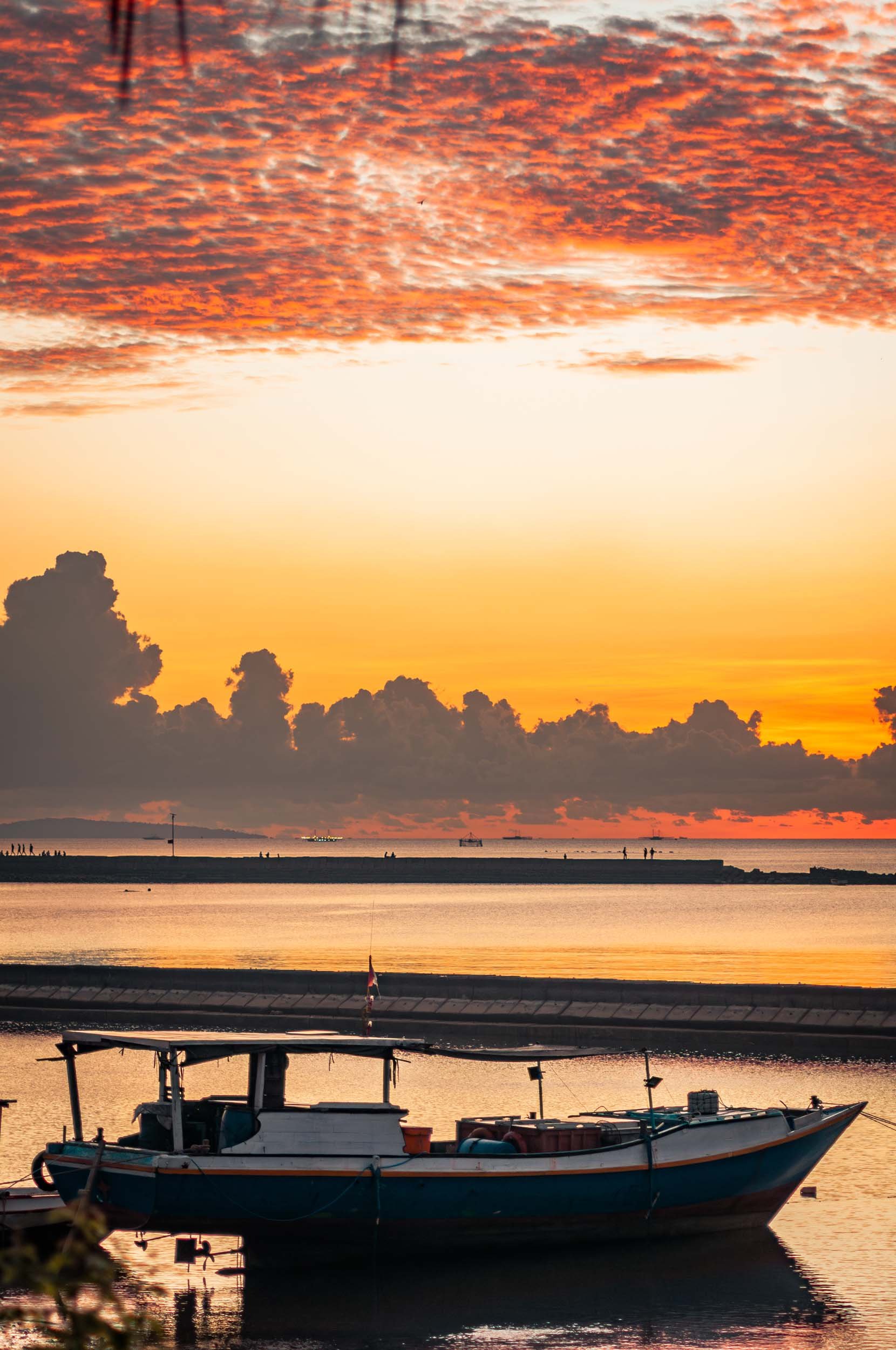 A boat docked in calm water during a vibrant sunset with orange, pink, and purple clouds in the sky.