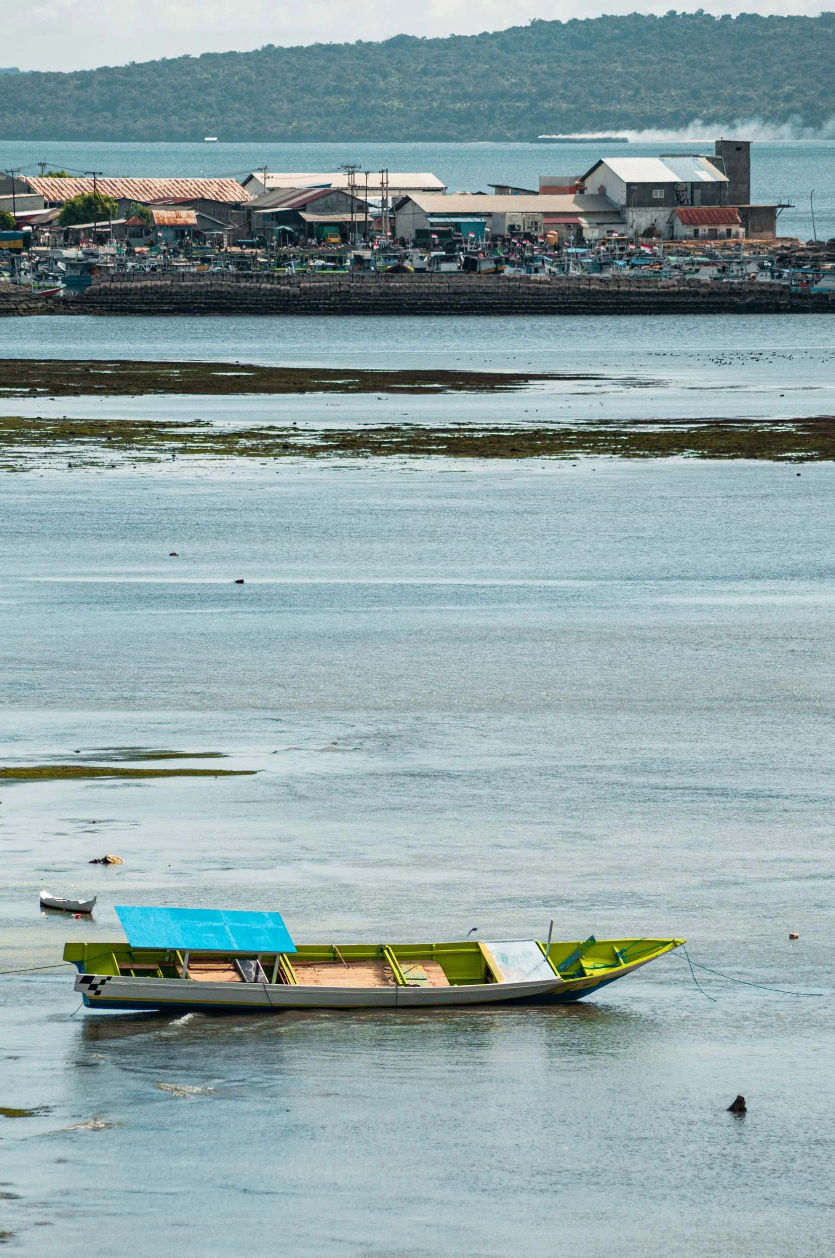 A partially submerged boat on a calm body of water, with a coastal town and hills in the background.