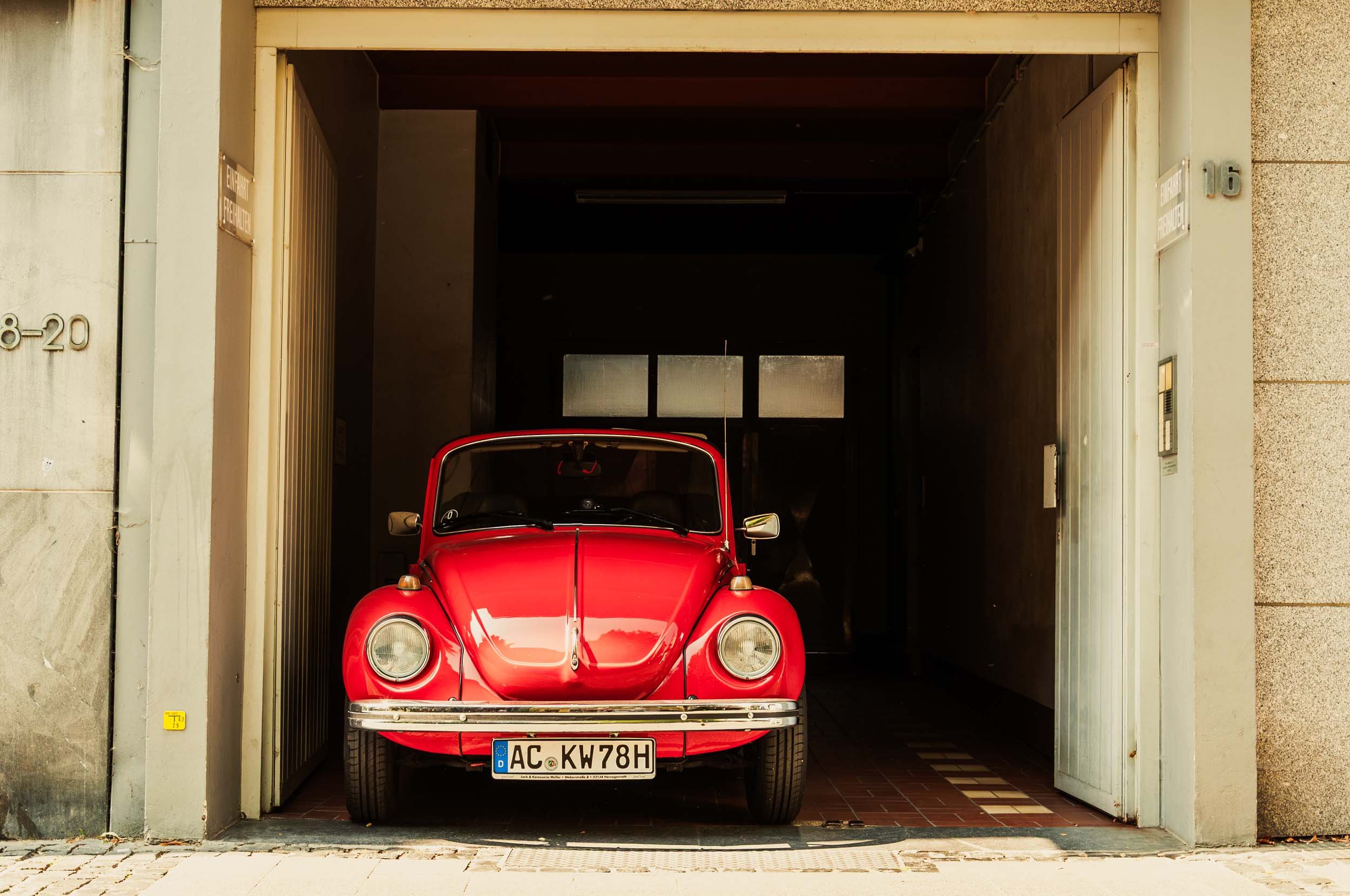 Red vintage Volkswagen Beetle in a garage with open door.