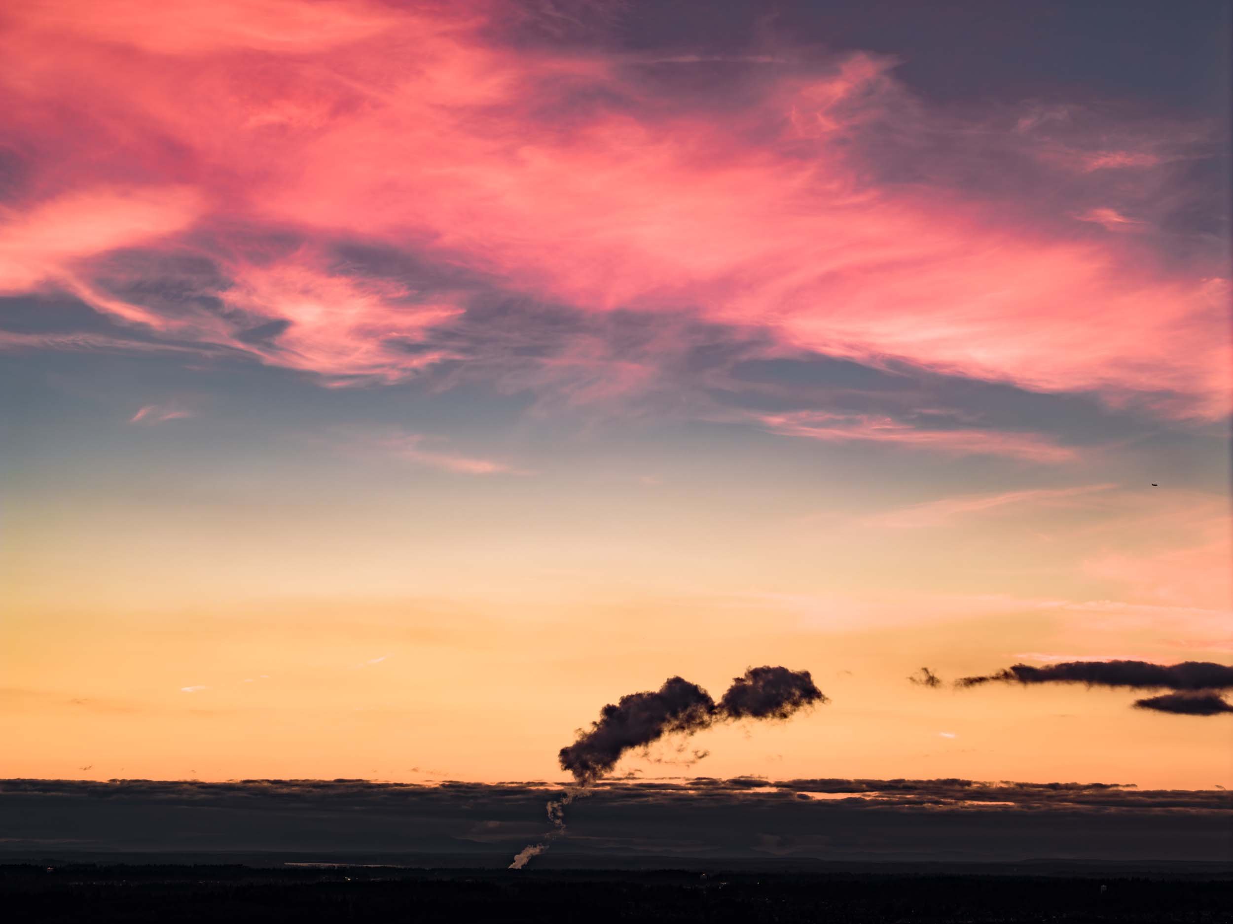 Colorful sunset sky with pink and orange clouds and dark smoke rising from a distant factory.