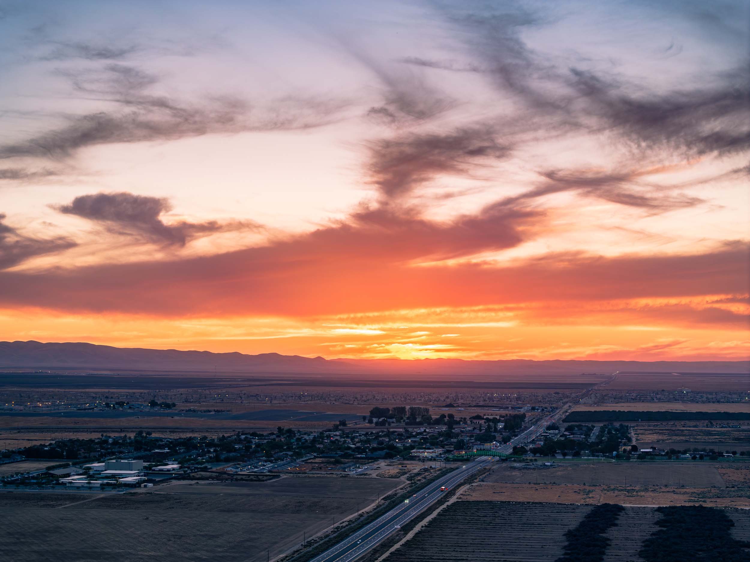 A sunset over a flat landscape with mountains in the background and a road stretching into the distance.