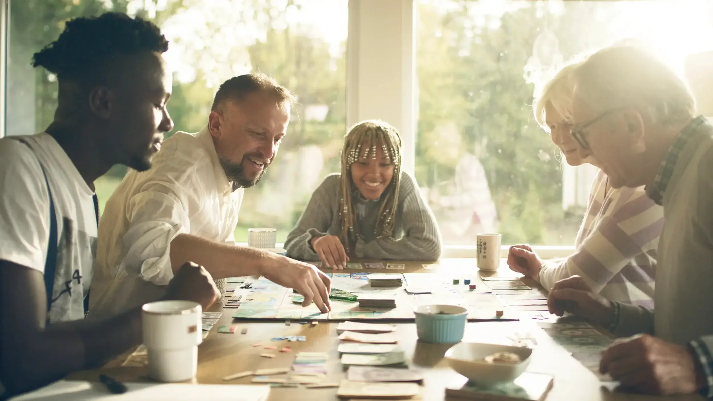 Gemini said A diverse group of five people of varying ages smile and laugh while playing a board game together around a sunlit wooden table.
