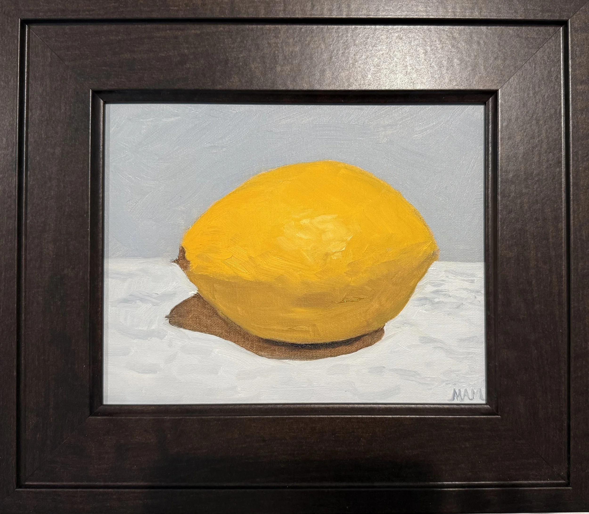 Painting of a yellow lemon on a white surface with a gray background, framed in a dark brown frame.