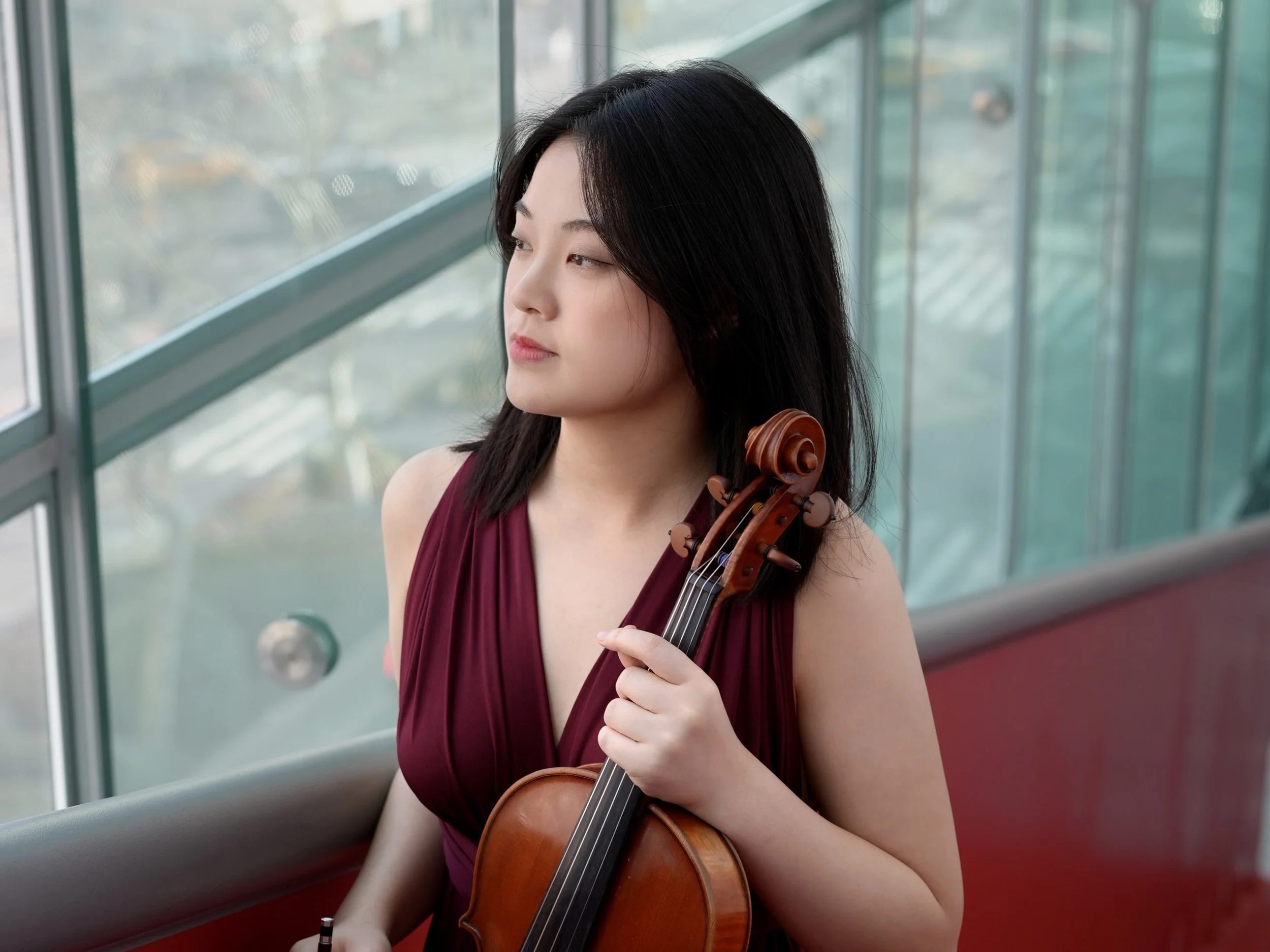 A musicain with black hair in a burgundy dress holding a viola