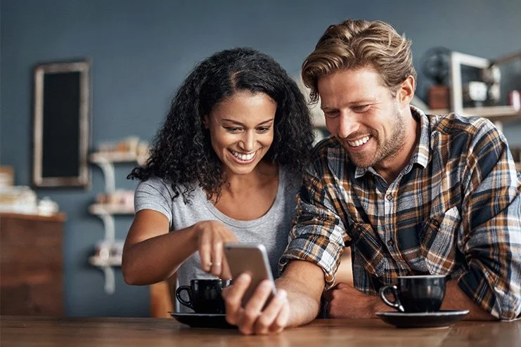 A happy couple looking at a smartphone together in a cozy cafe.