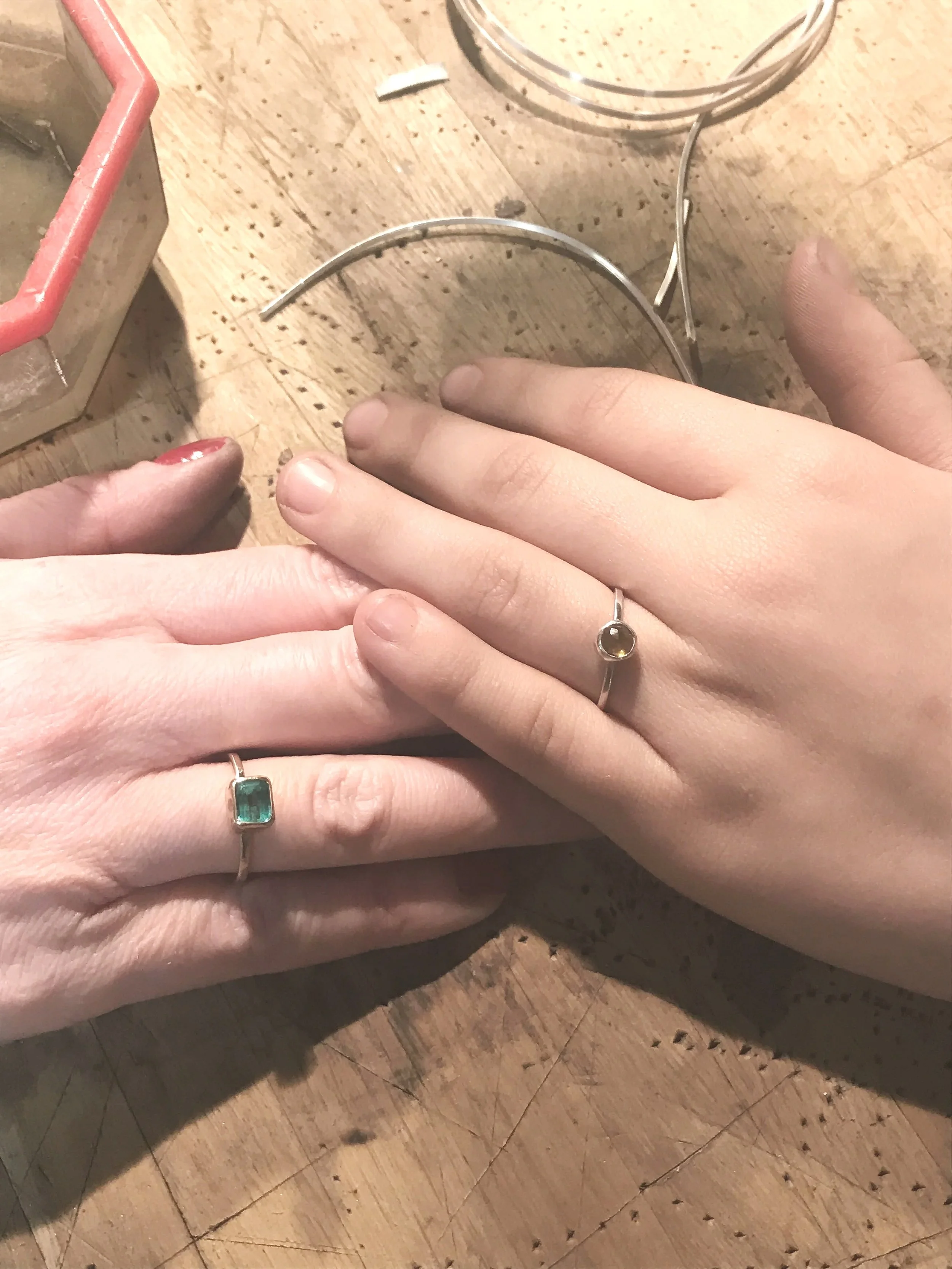 Two hands with decorated nails and rings resting on a wooden surface, with jewelry pieces nearby.