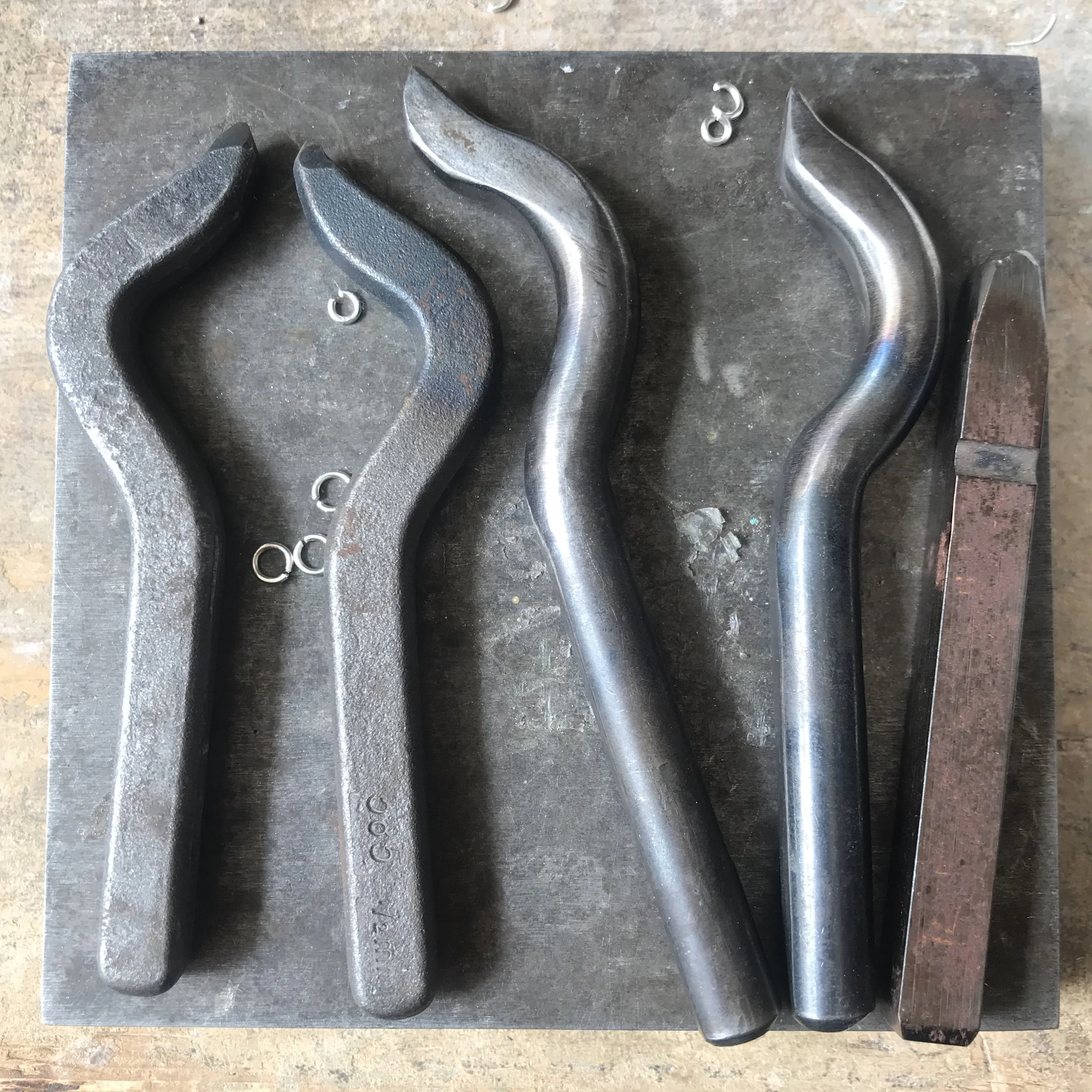 Metal molds and small metal rings placed on a metal work surface, likely in a workshop or manufacturing setting.