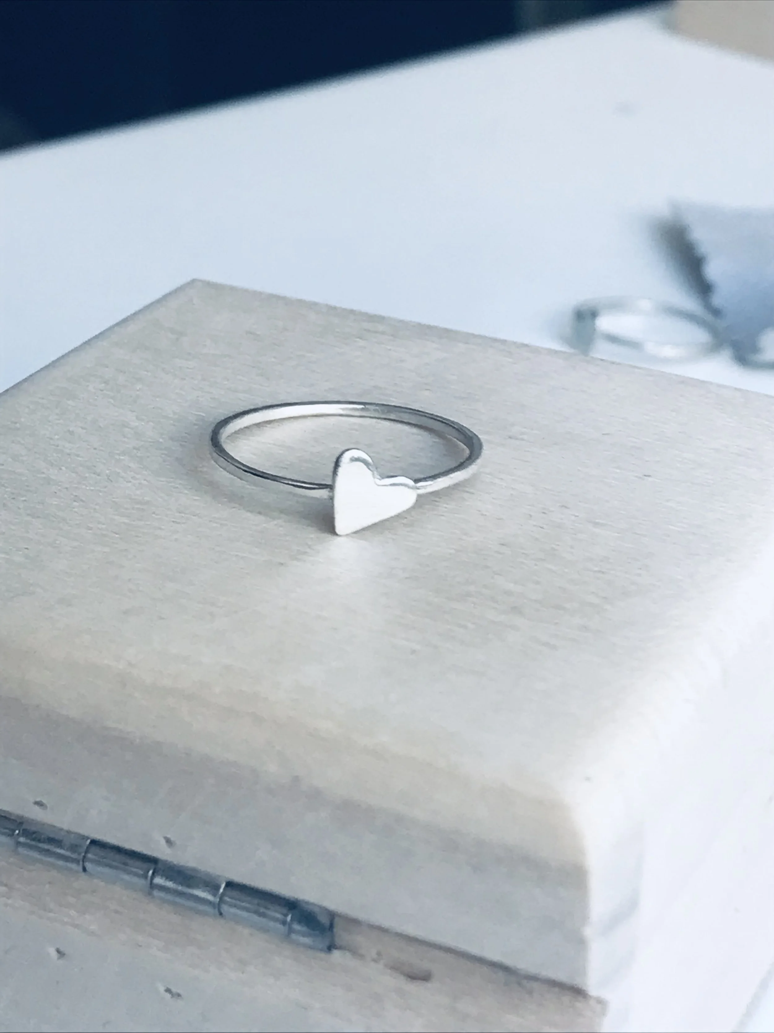 Close-up of a metallic jewelry display with a silver heart-shaped ring and a plain silver band, on a white stand with a curved base.