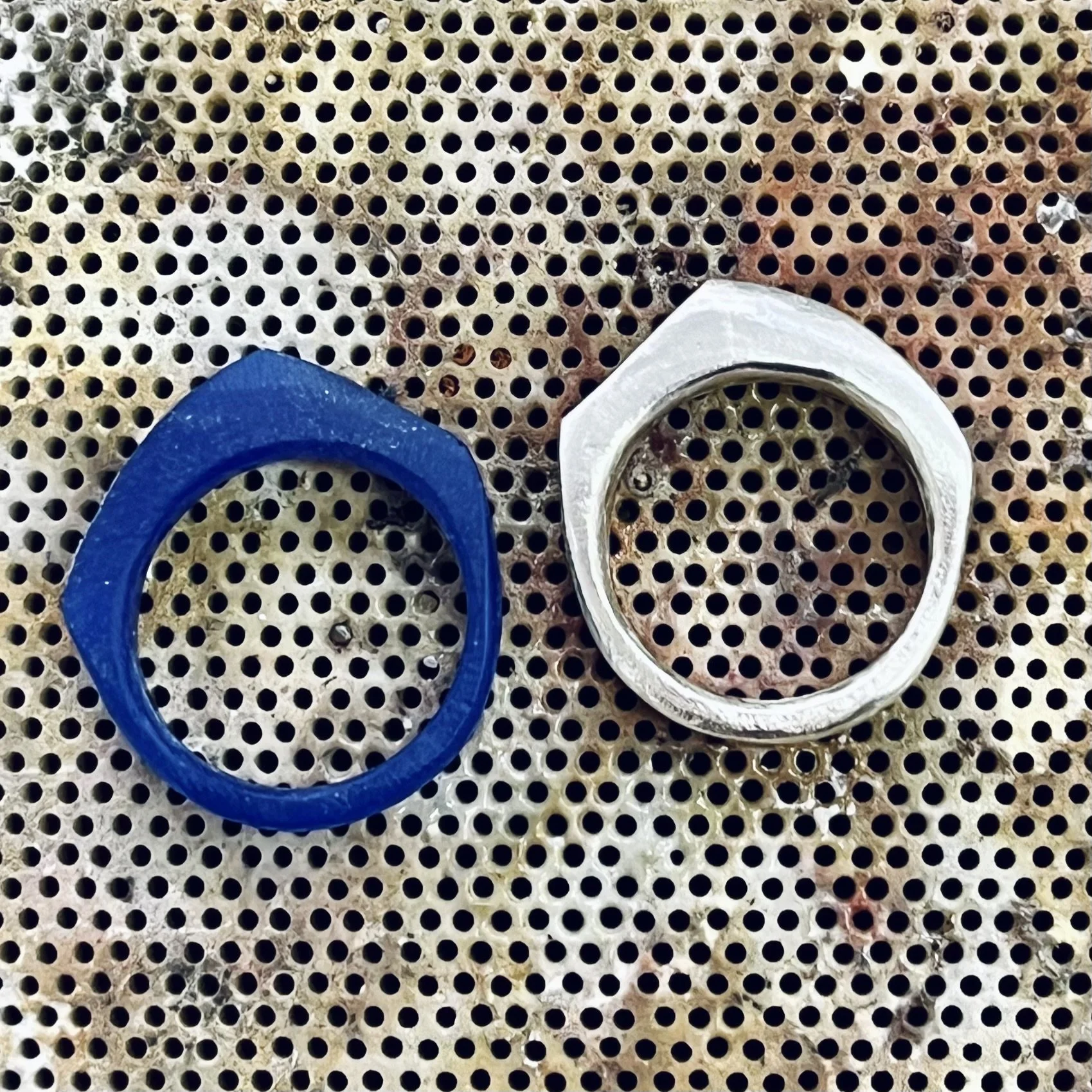 A perforated metal surface with a blue rubber ring and a white plastic or ceramic ring placed on top.