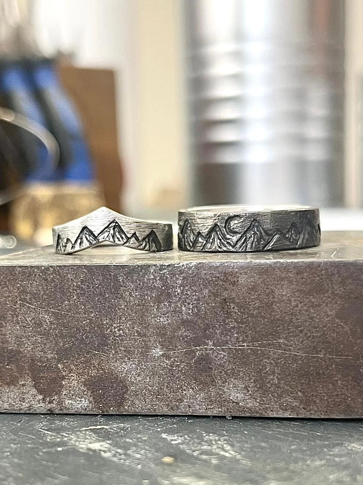 Two rings with mountain designs on a work surface in a jewelry studio.