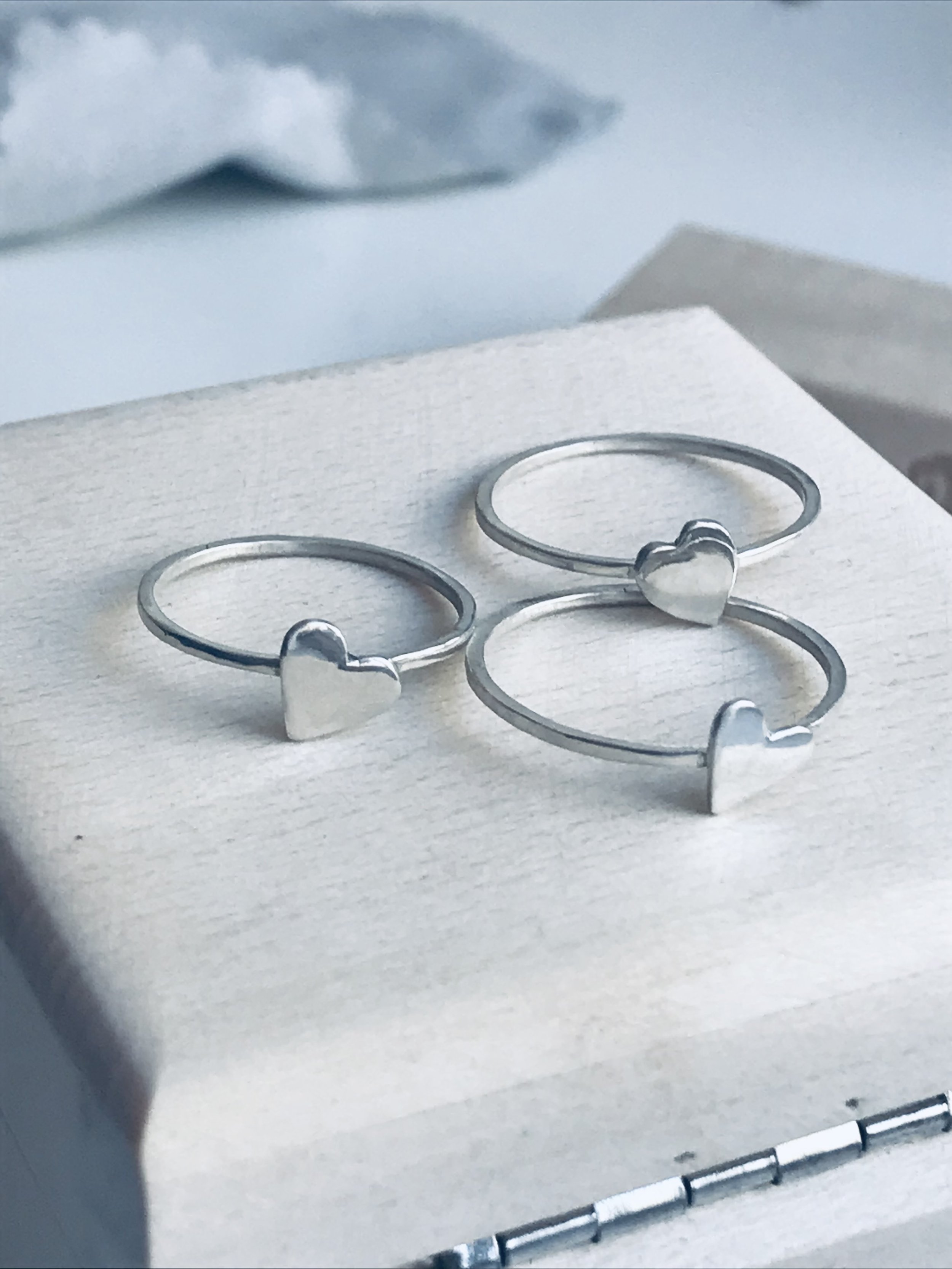 Three silver rings with heart-shaped accents placed on a white surface, with a white box behind them.