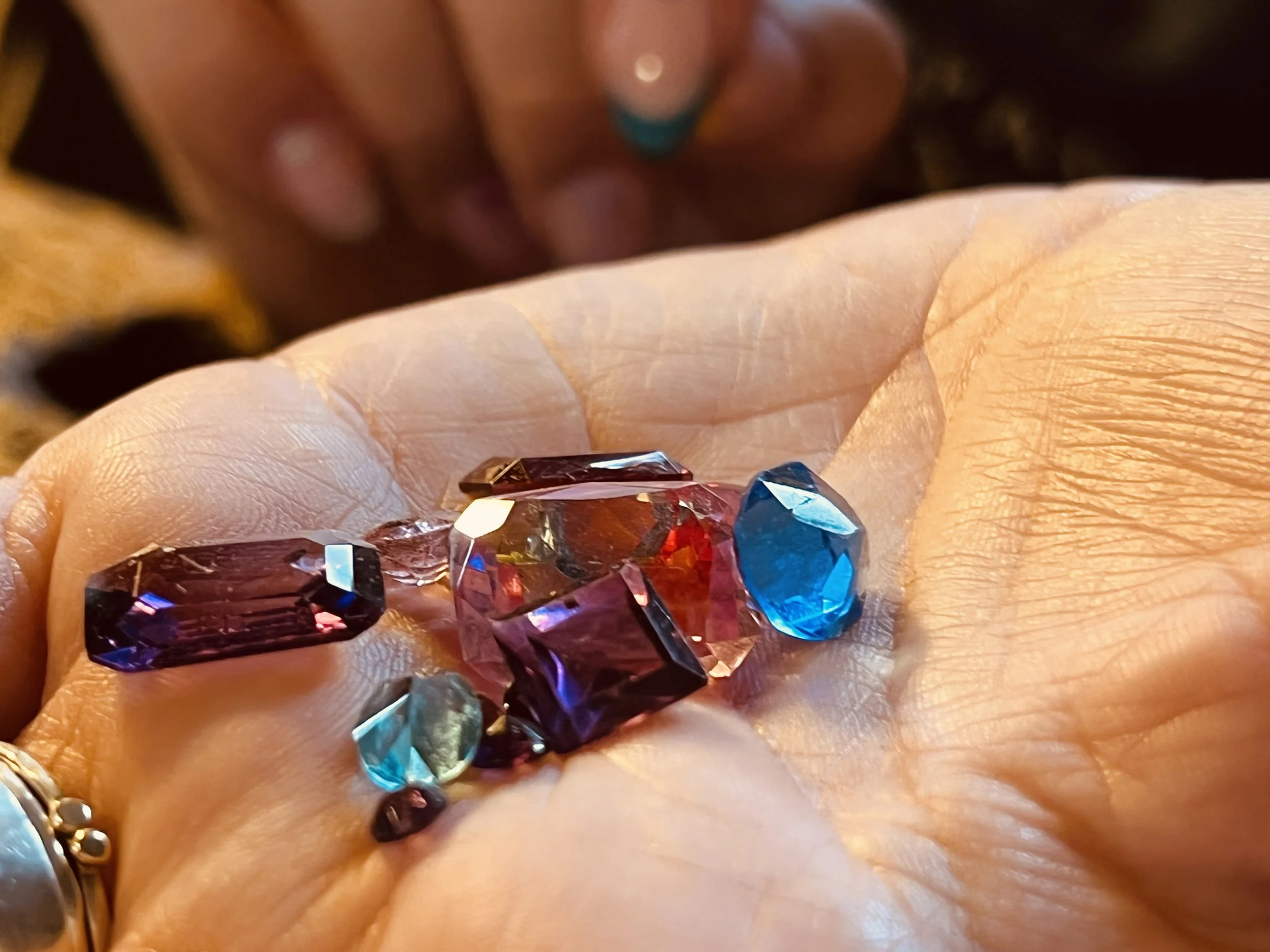 Close-up of a hand with colorful gemstones on the fingers, with a blurred background.