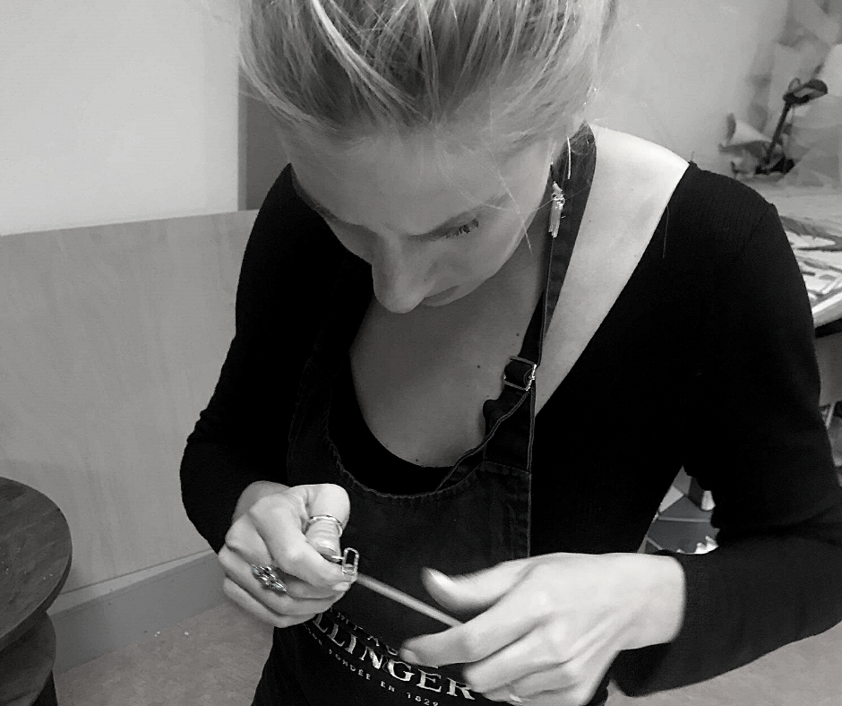 A woman with blonde hair doing a craft or jewelry making project, focused on her hands holding a small tool.