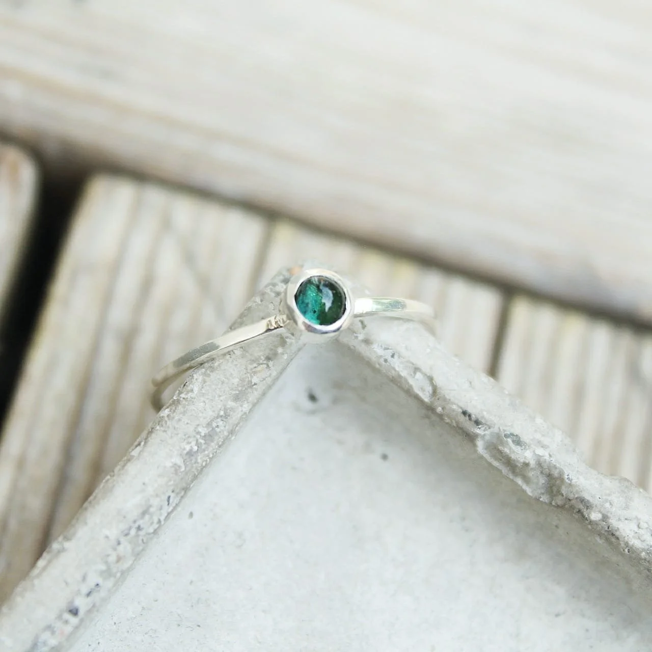 Silver ring with round green gemstone on a concrete surface with wooden background.