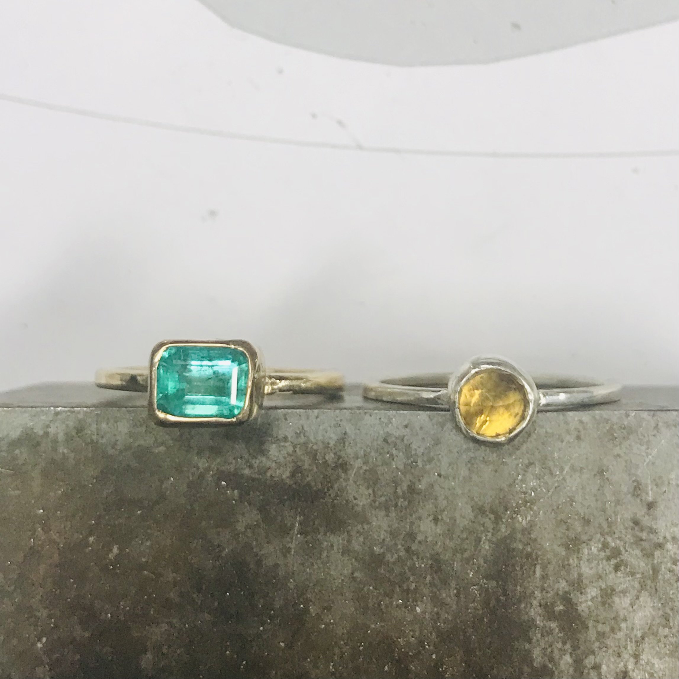Close-up of four rings with gemstones, placed on a dark surface, with a white background.