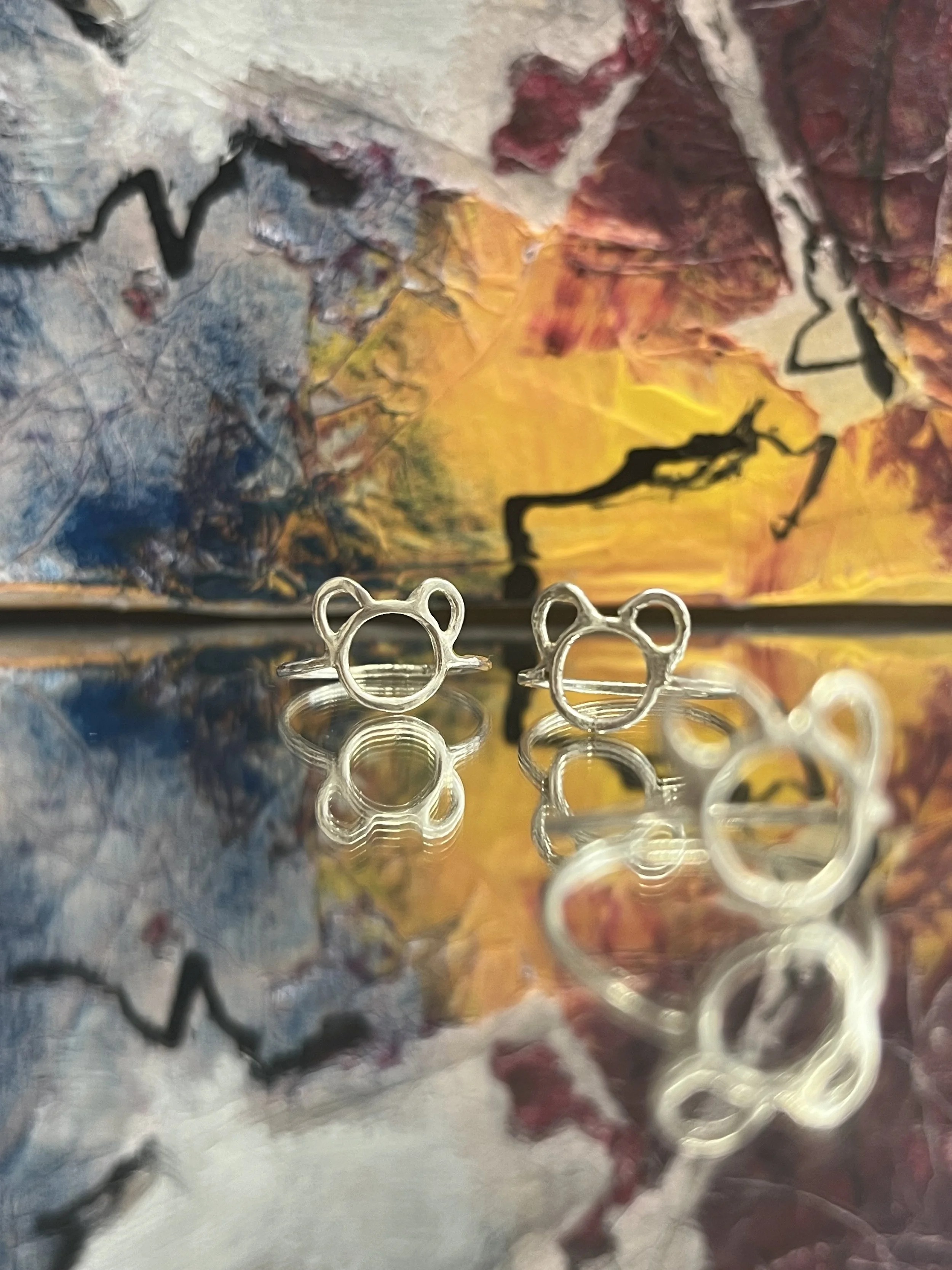 Close-up of a metallic surface with a reflection of a colorful, abstract painting and small Mickey Mouse-shaped rings or objects in the foreground.