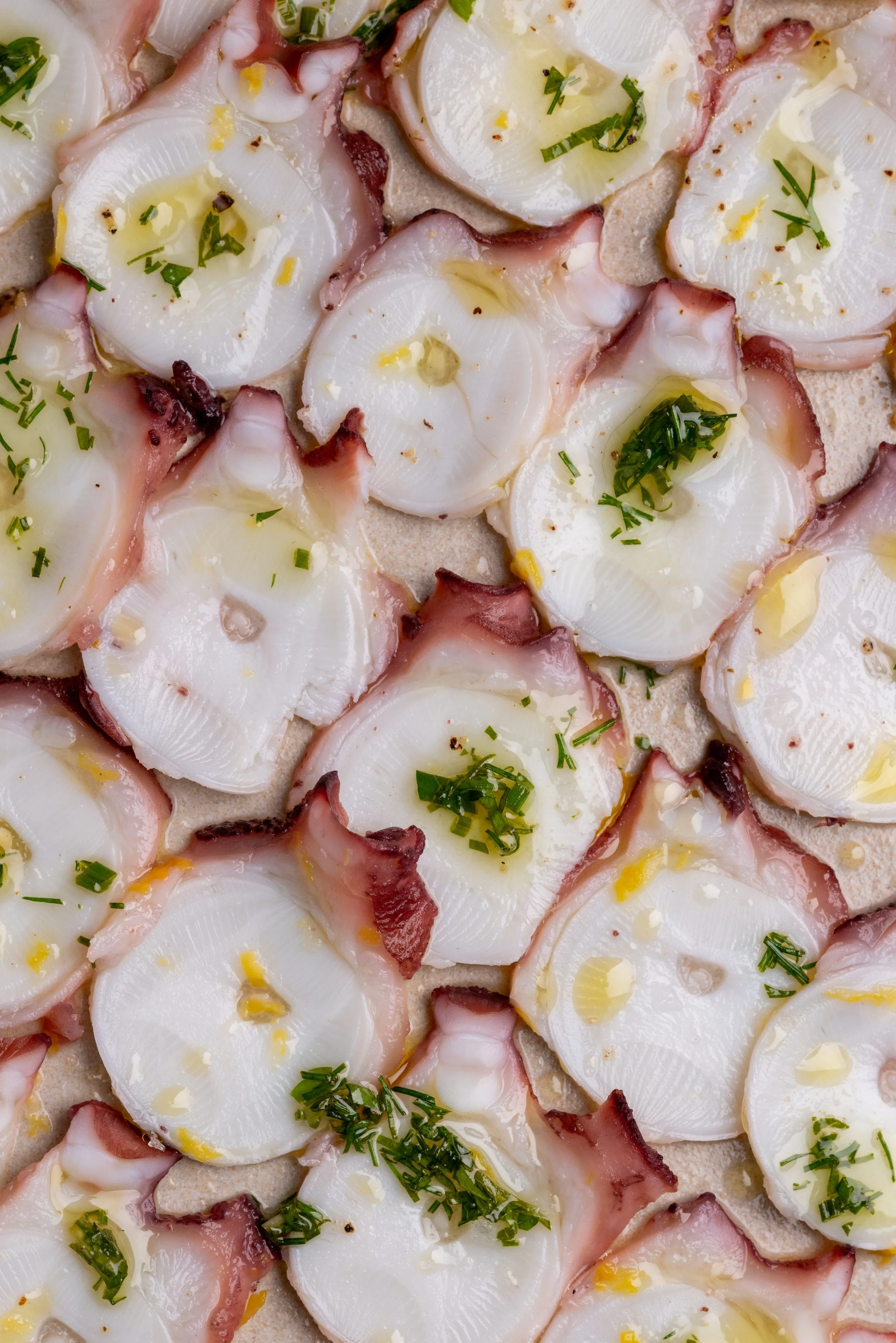 Close-up of octopus carpaccio topped with chopped herbs, lemon juice, and olive oil.