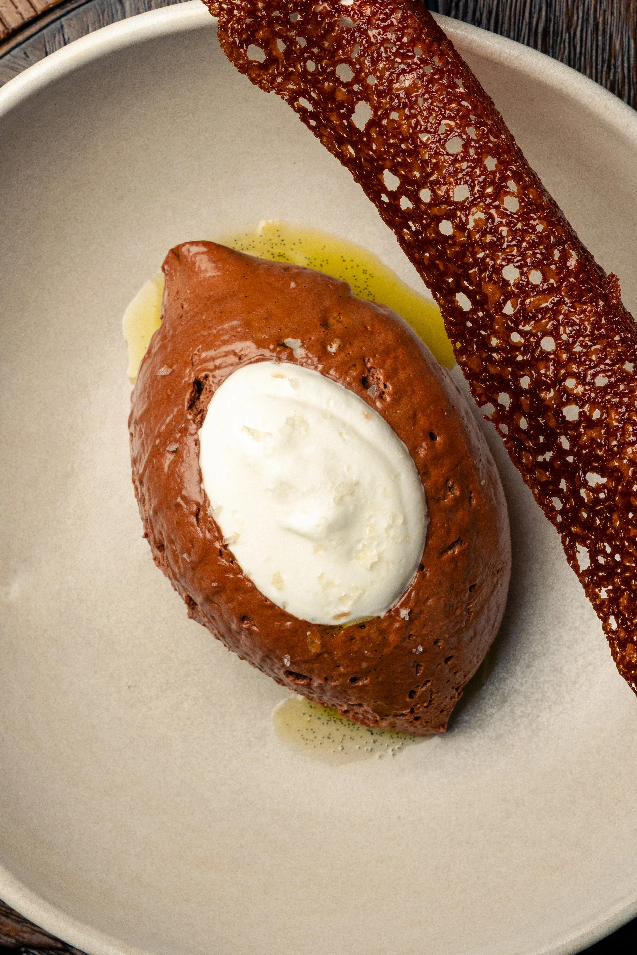 Baked stuffed tomato with a dollop of sour cream or cream on top, drizzled with oil, and a crispy lace tuile on a light-colored plate.