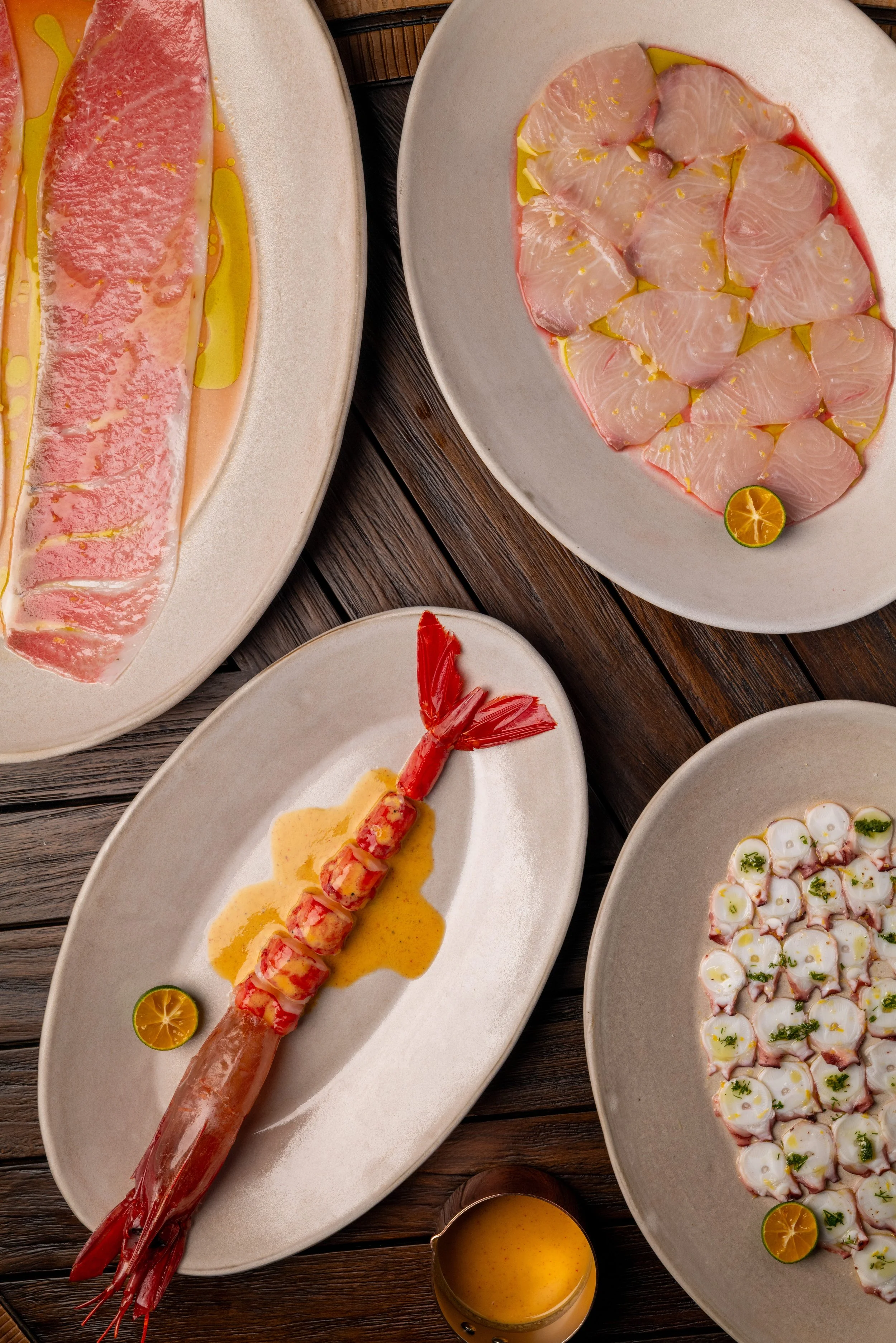 Assorted seafood dishes on platter, including slices of raw fish, cooked shrimp, and octopus with garnishes.