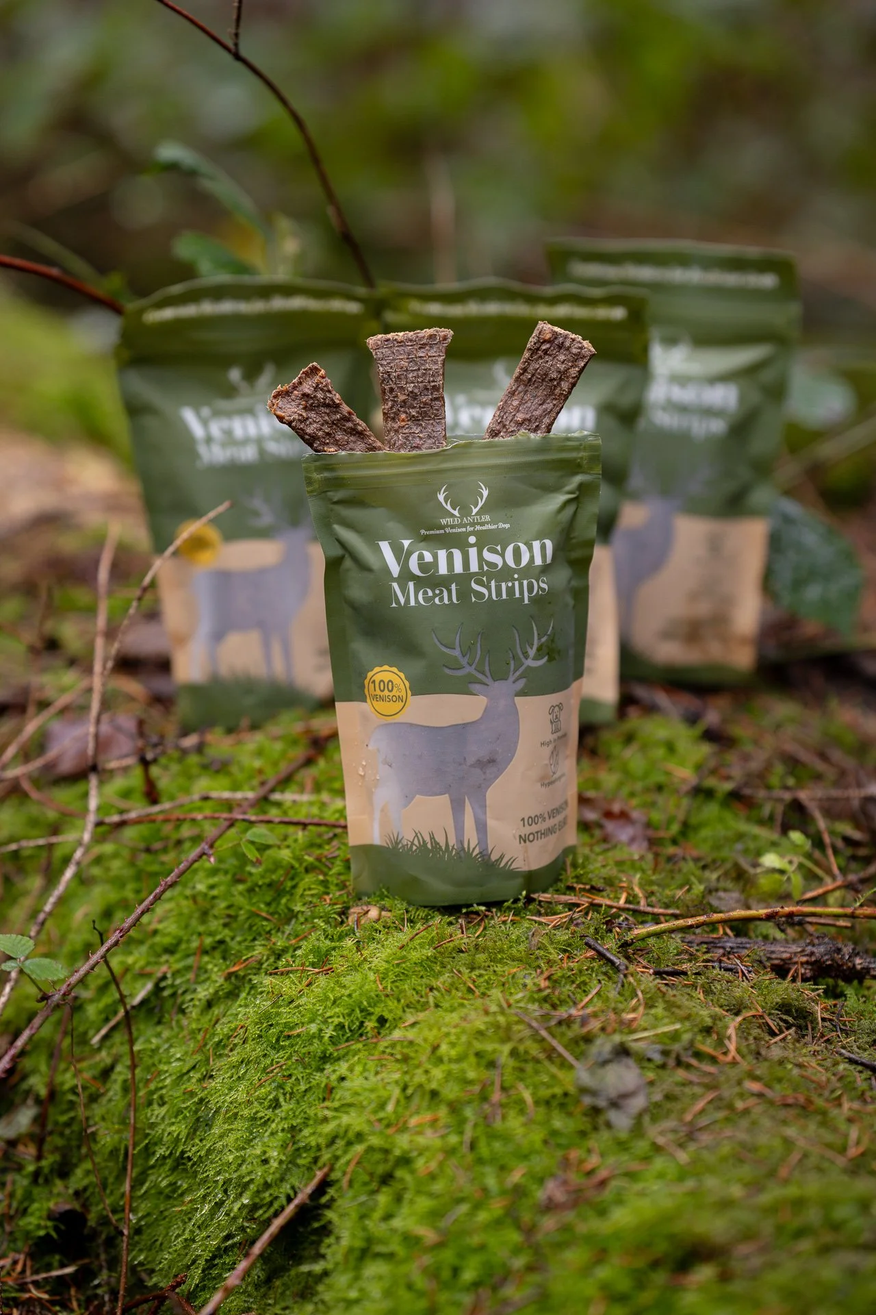 3 packs of Wild Antler venison meat strips posed on a log with leaves and moss