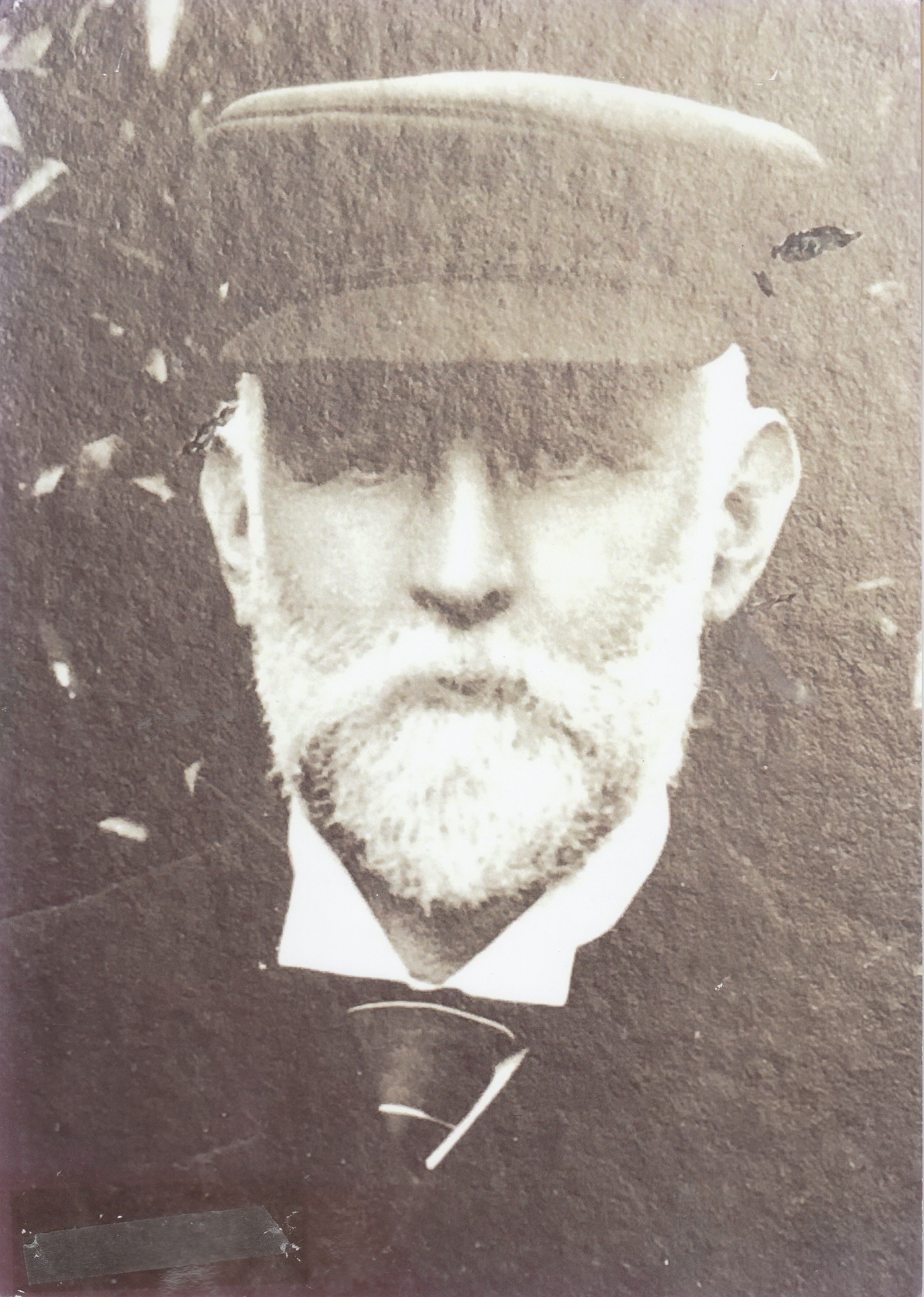 Black and white photograph of a man wearing a hat and a suit with a bow tie, with a beard and mustache, looking directly at the camera.