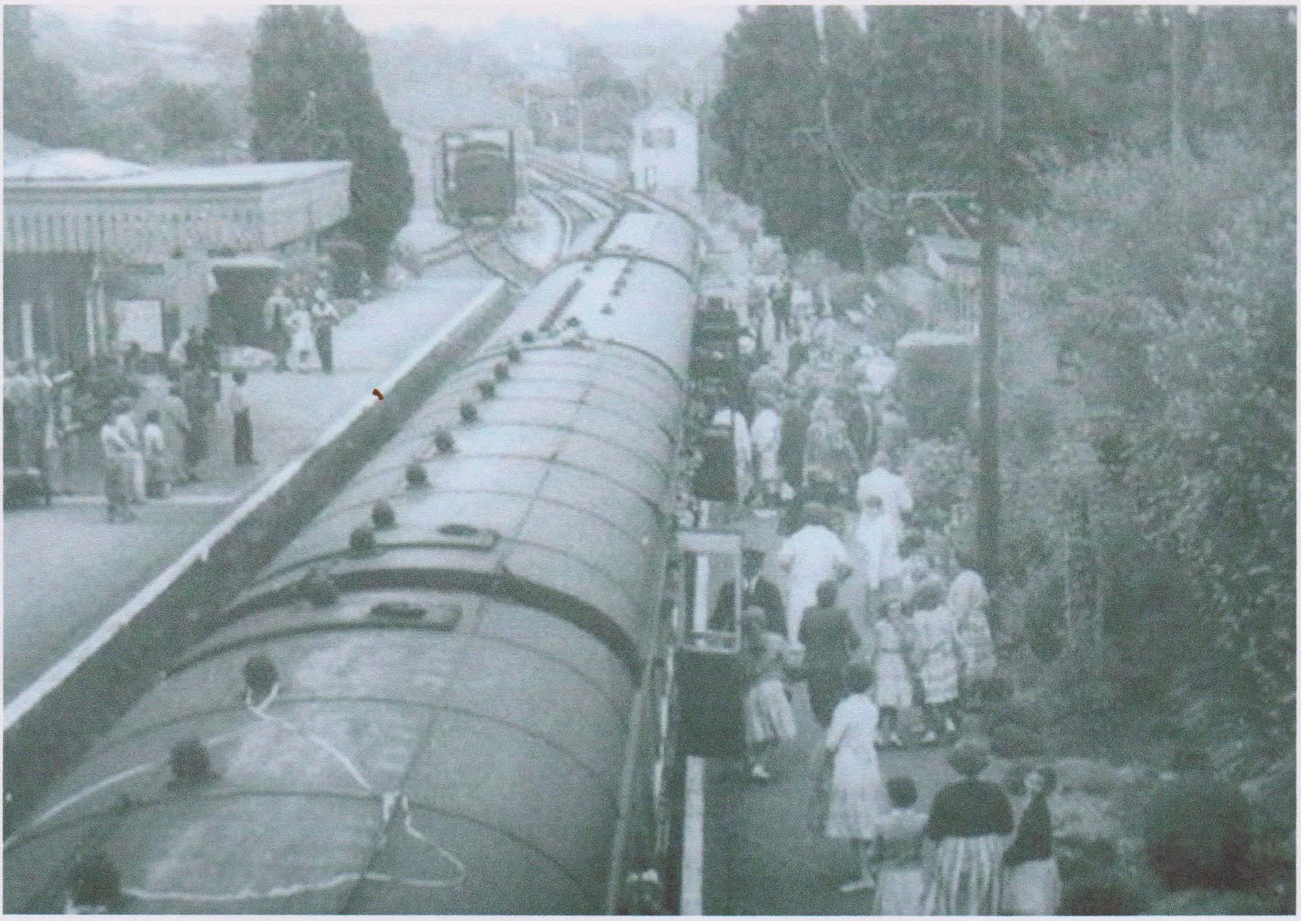 Black and white photo of people boarding and waiting near a train on a station platform.