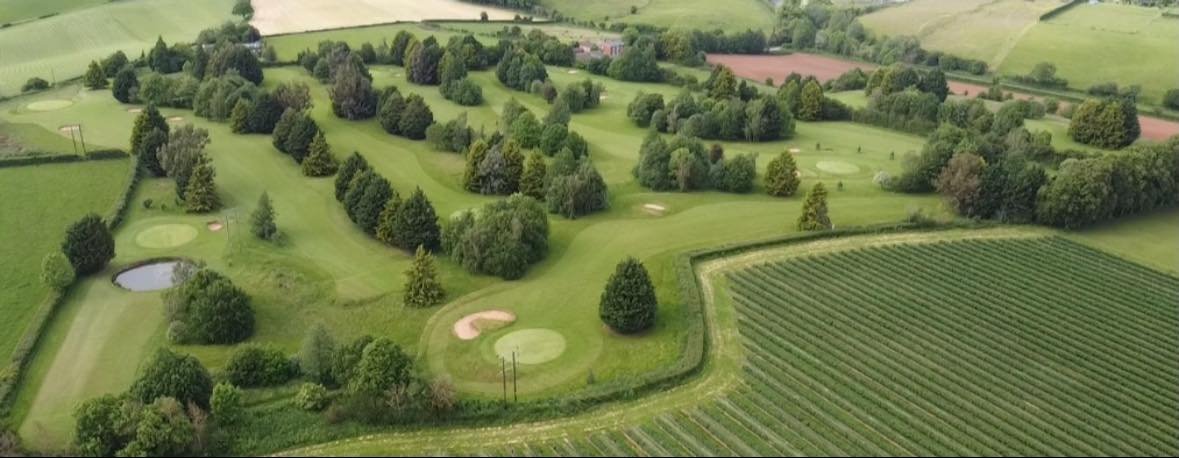 Aerial view of a golf course surrounded by trees and farmland, with several sand traps and water hazards.