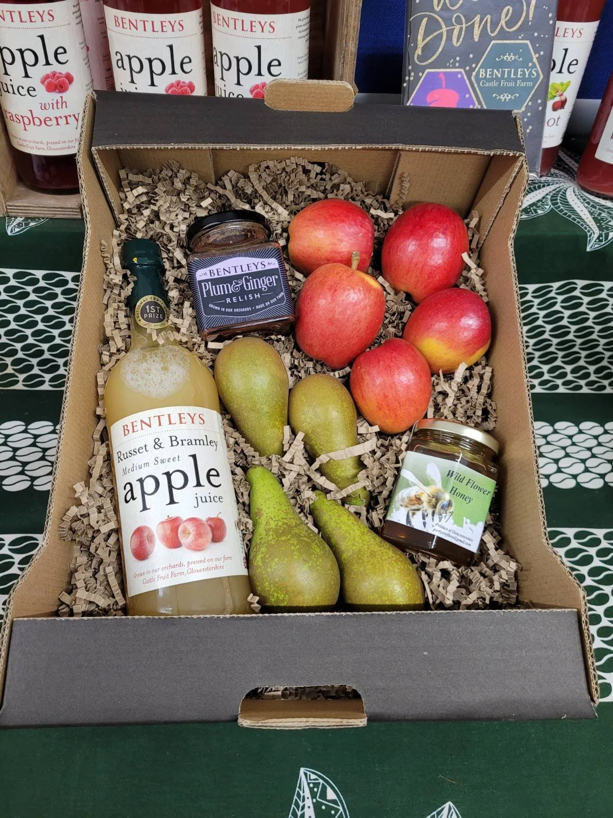 A gift box containing apples, pears, honey, apple juice, a small jar of plum and ginger relish, and a jar of wildflower honey.