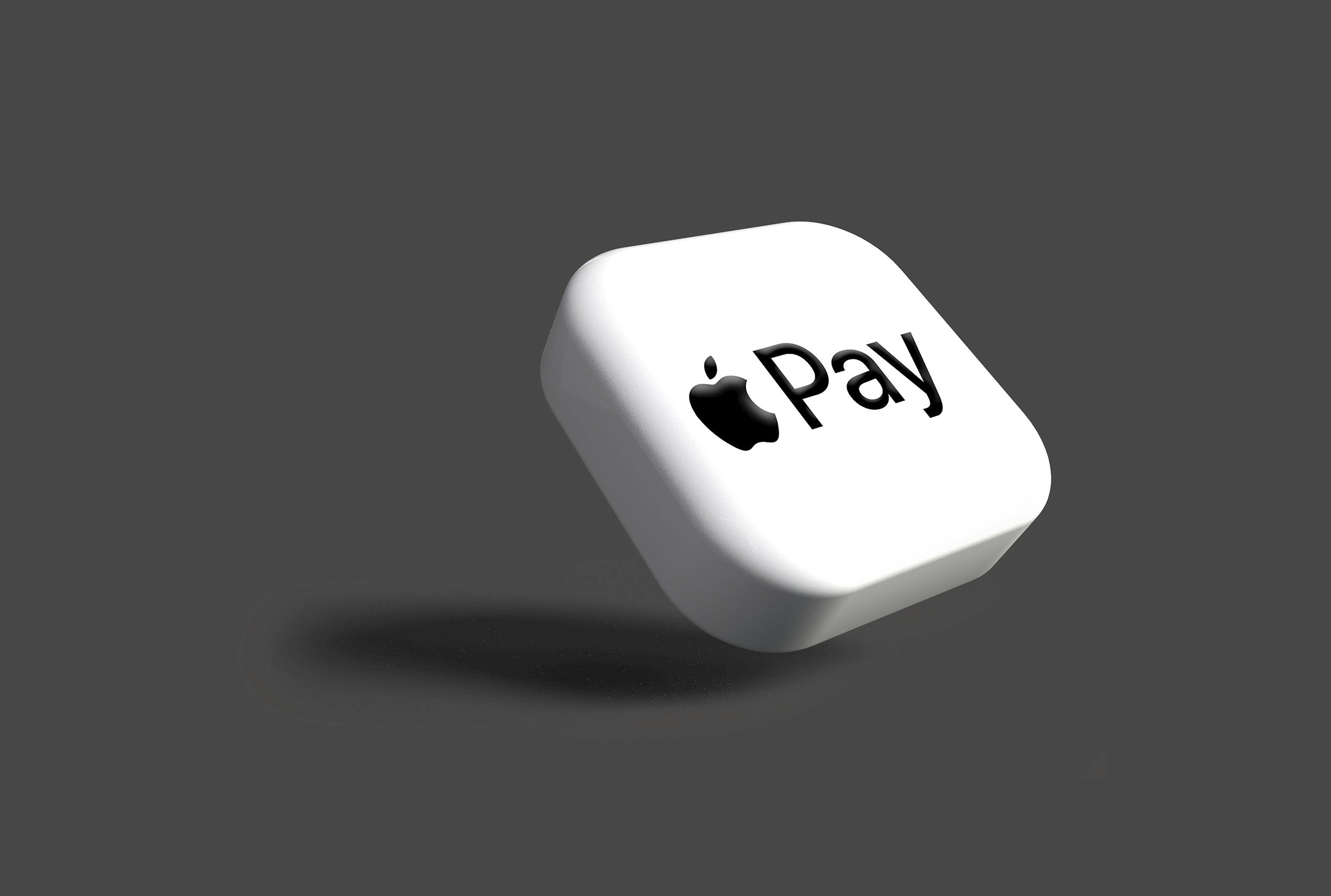 A white cube with the Apple Pay logo on top, casting a shadow on a gray background.