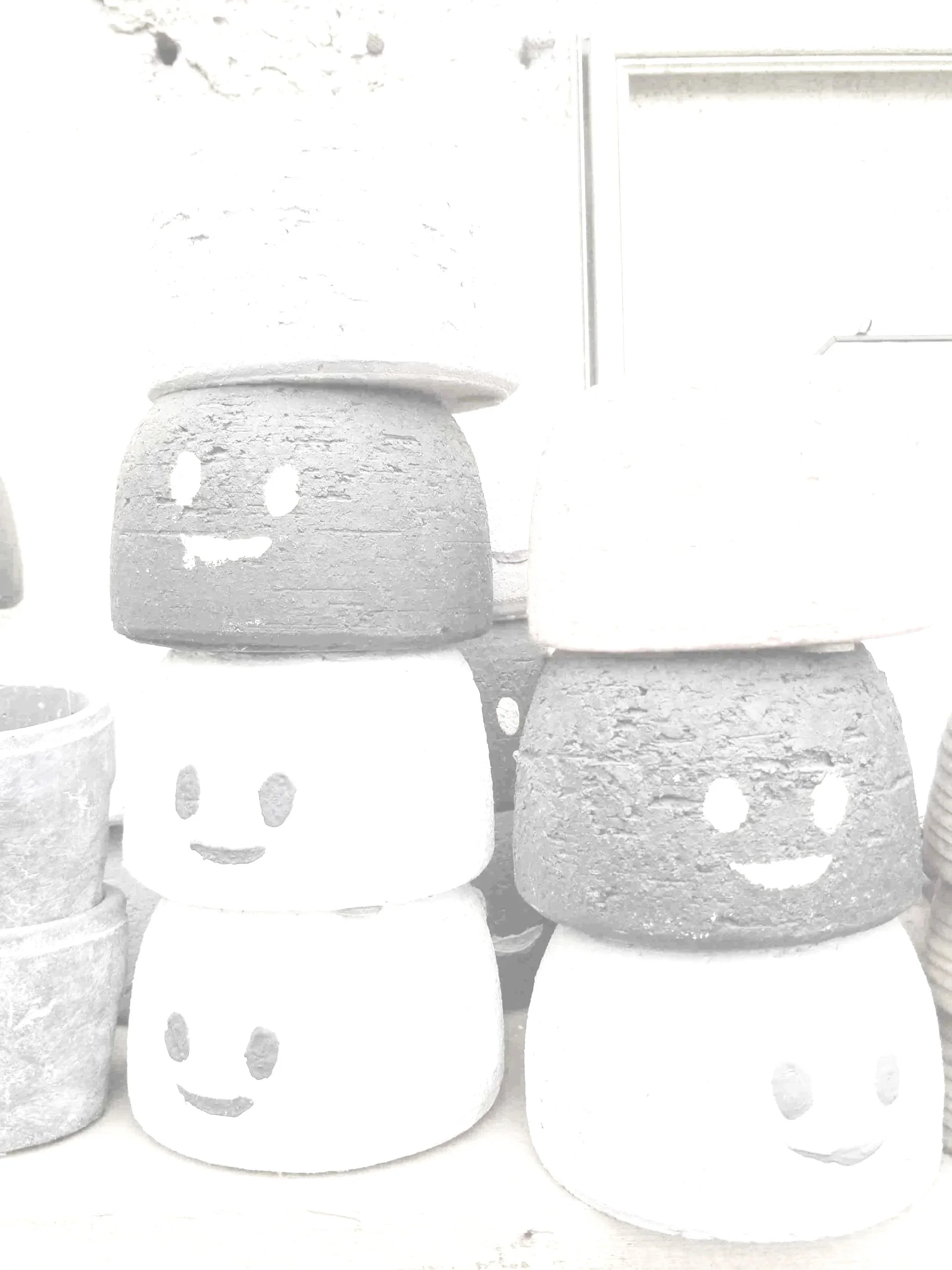 Stacks of white ceramic pots with smiley face cutouts, some with multiple holes, arranged on a surface.