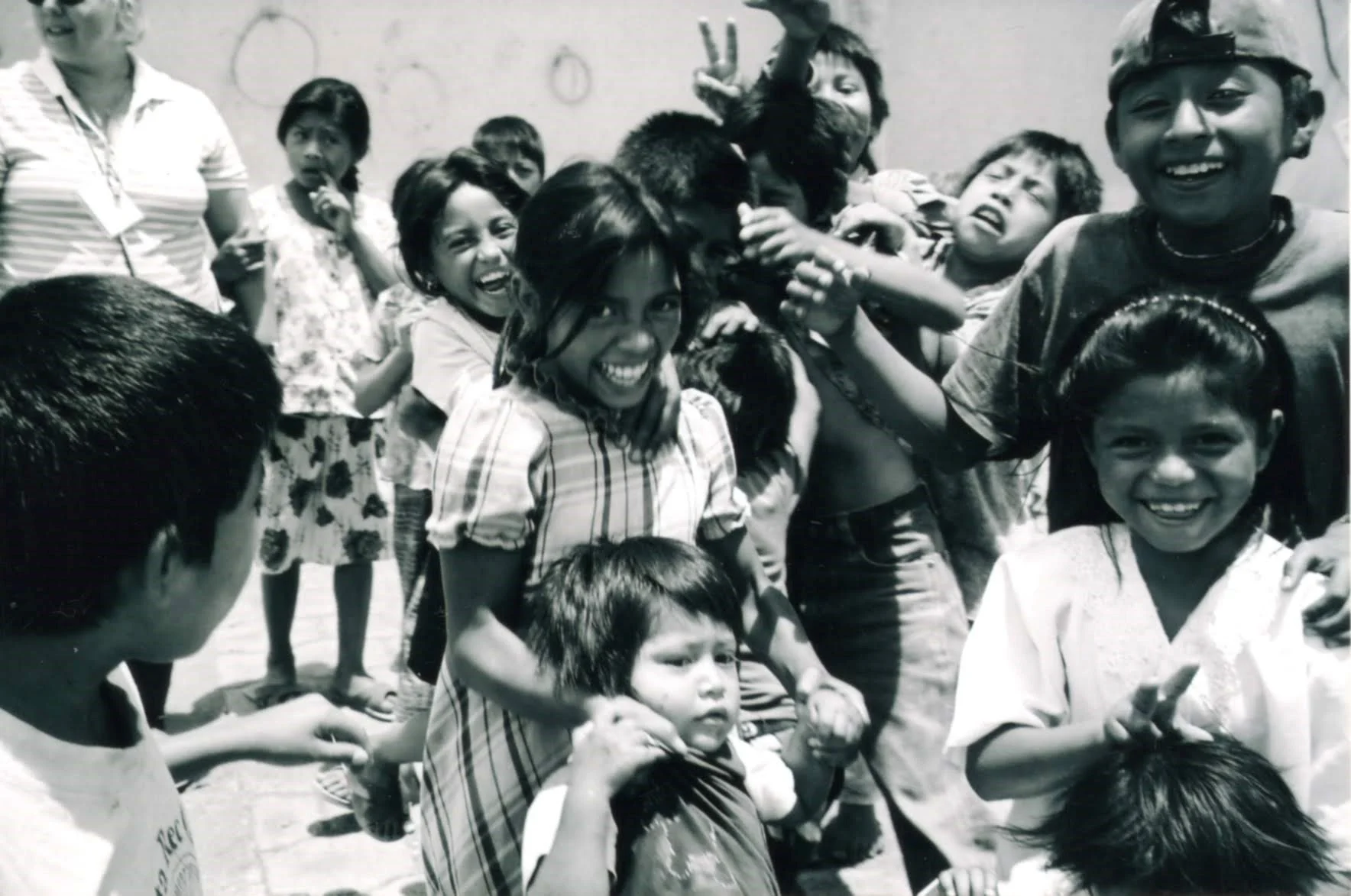 Group of children and a woman smiling and playing together outdoors, some holding hands, in black and white photograph.