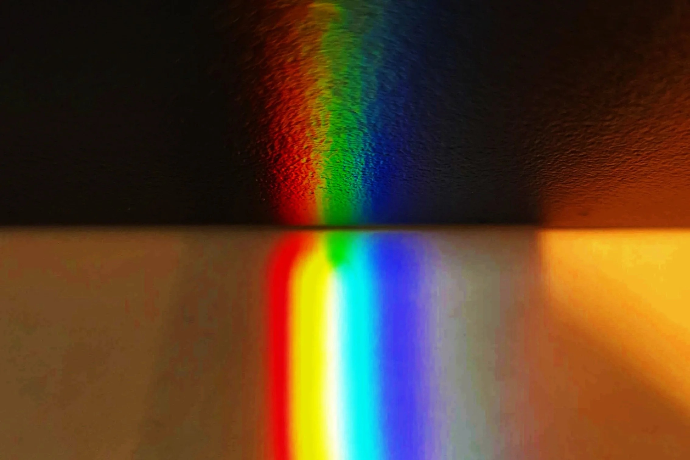 A rainbow spectrum reflected on a surface, displaying red, orange, yellow, green, blue, and violet colors gradually blending into each other.