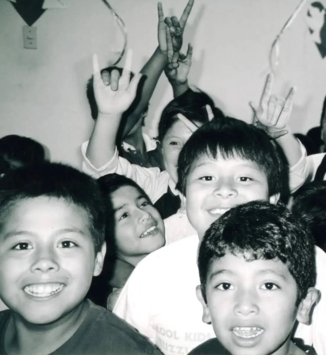 Group of smiling children in a crowded setting making various hand gestures, black and white photo