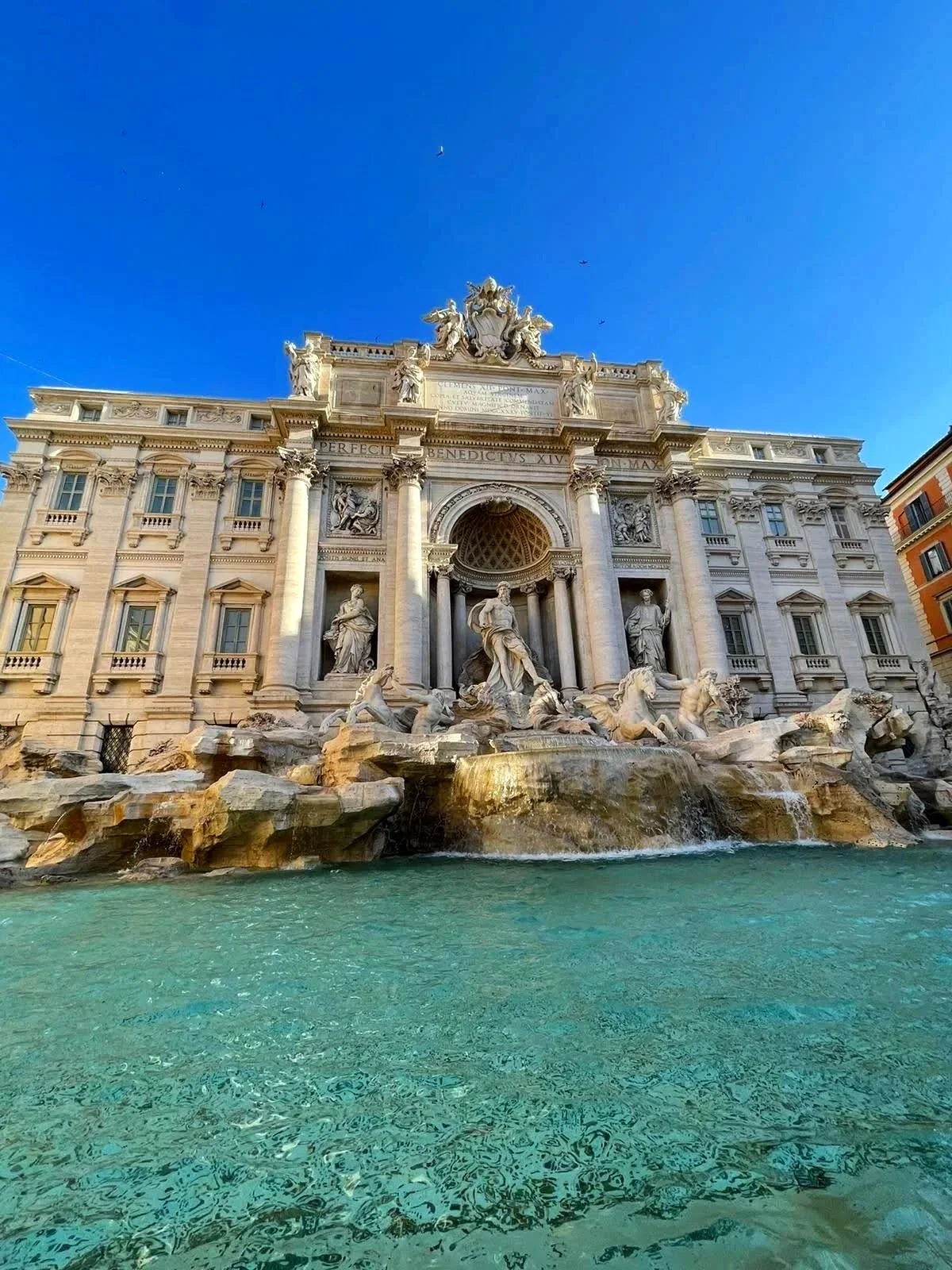 View of Trevi Fountain in Rome, Italy, with detailed sculptures and cascading water against a clear blue sky.