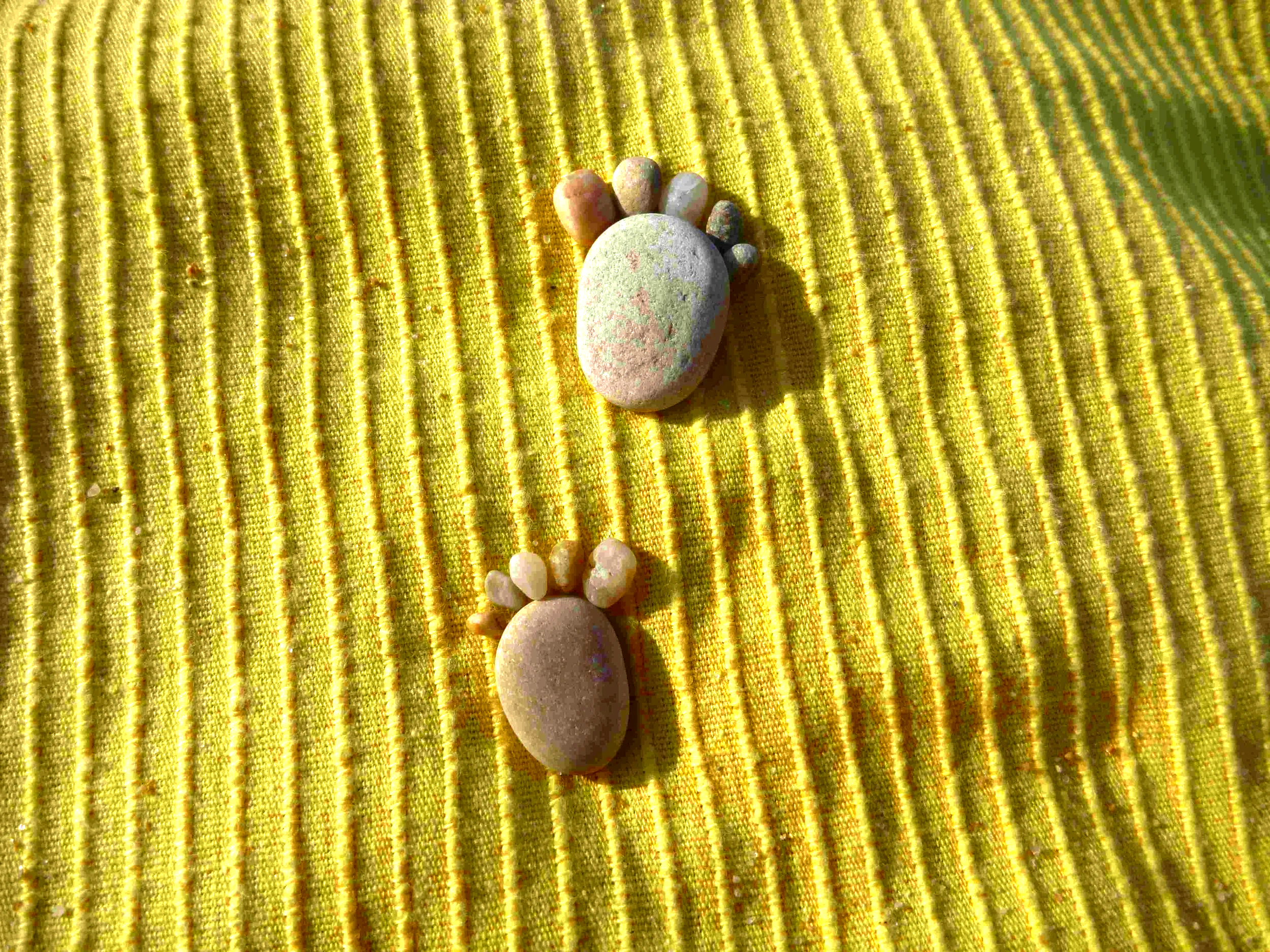 A collection of variously sized and shaped smooth stones arranged as footsteps on a bright yellow textured fabric background.