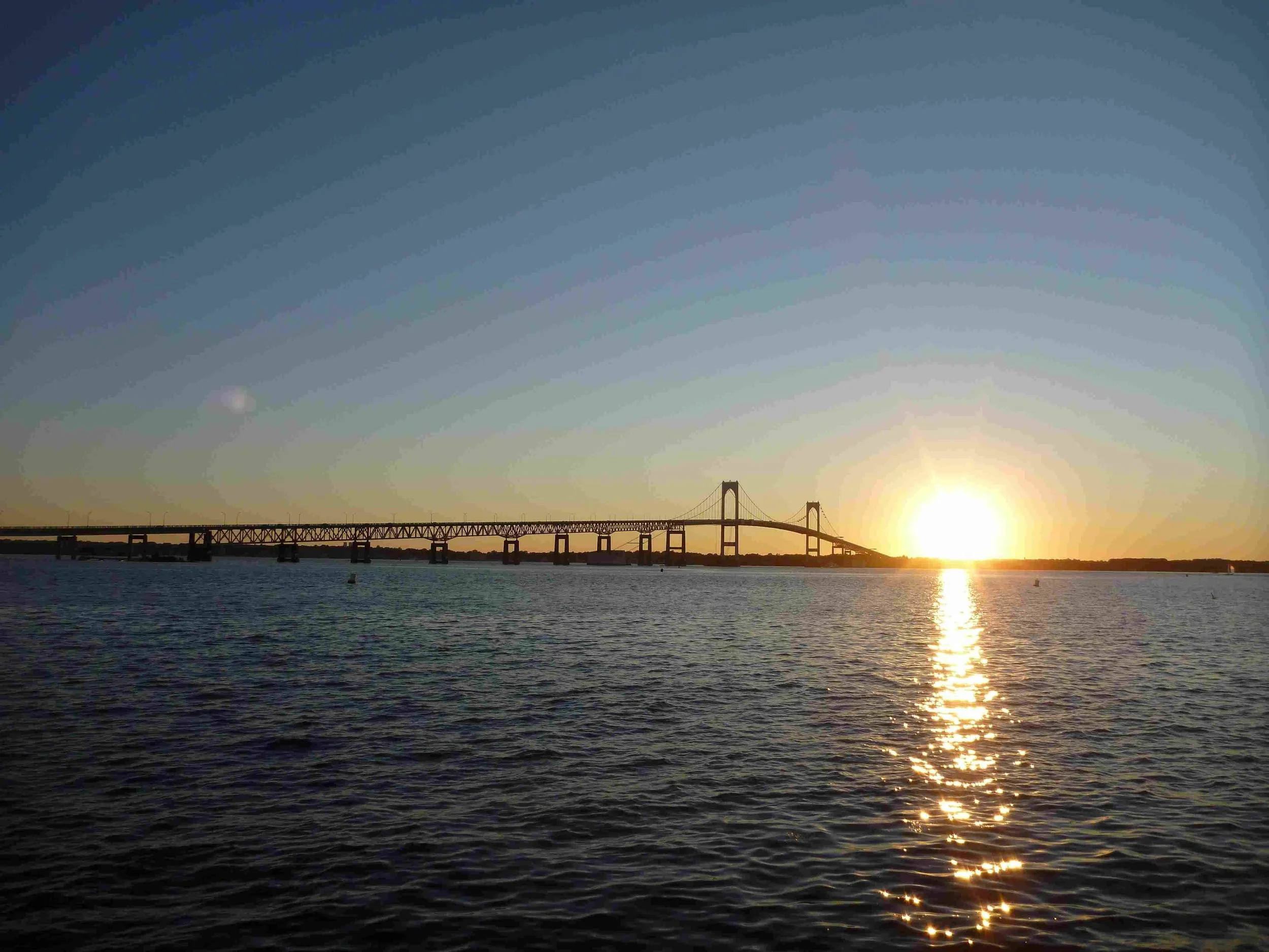 Sunset over a body of water with a bridge in the distance. The Newport Bridge, Newport Rhode Island