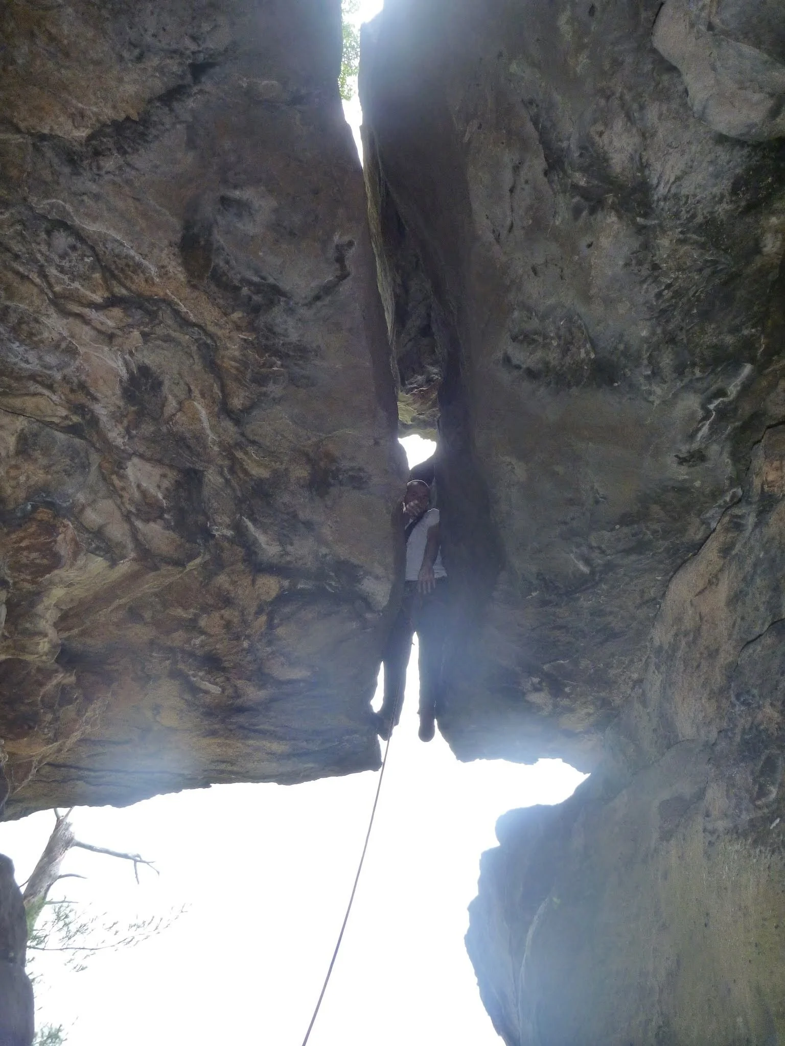 Person rappelling down a narrow rocky crevice with a rope, surrounded by large rocks and cliffs, in a natural outdoor setting.